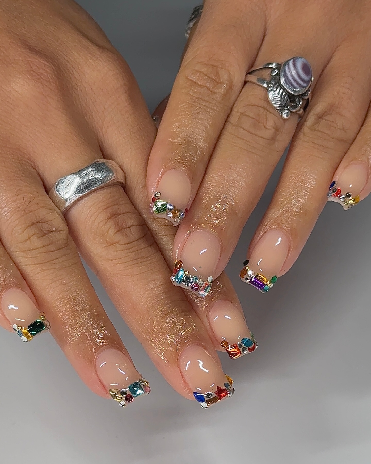 Sheer nude square nails edged with a dense border of multicolour rhinestones along the tips