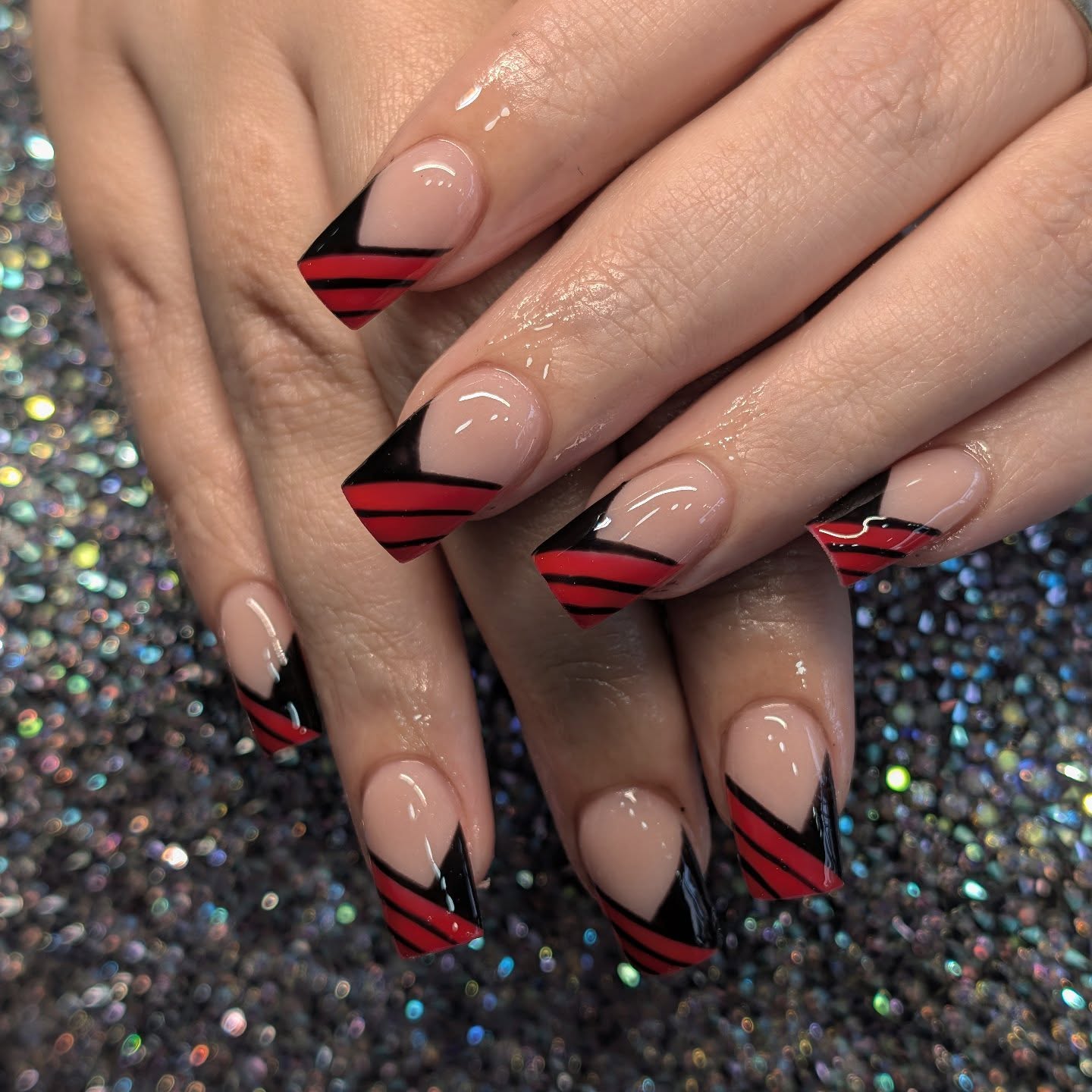 Nude stiletto nails with bold red and black diagonal geometric French tip designs