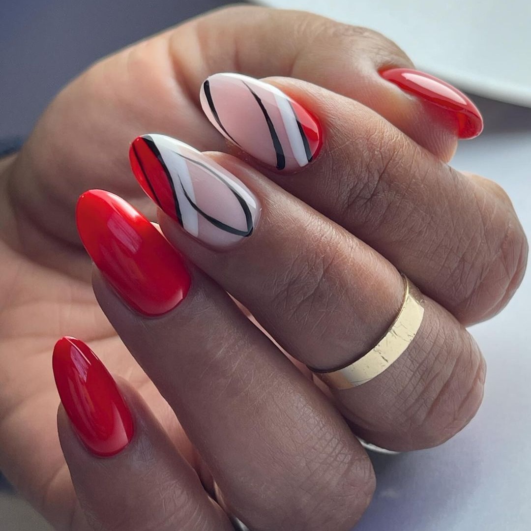 Long oval nails in glossy red with a white accent nail featuring curved black and red abstract lines