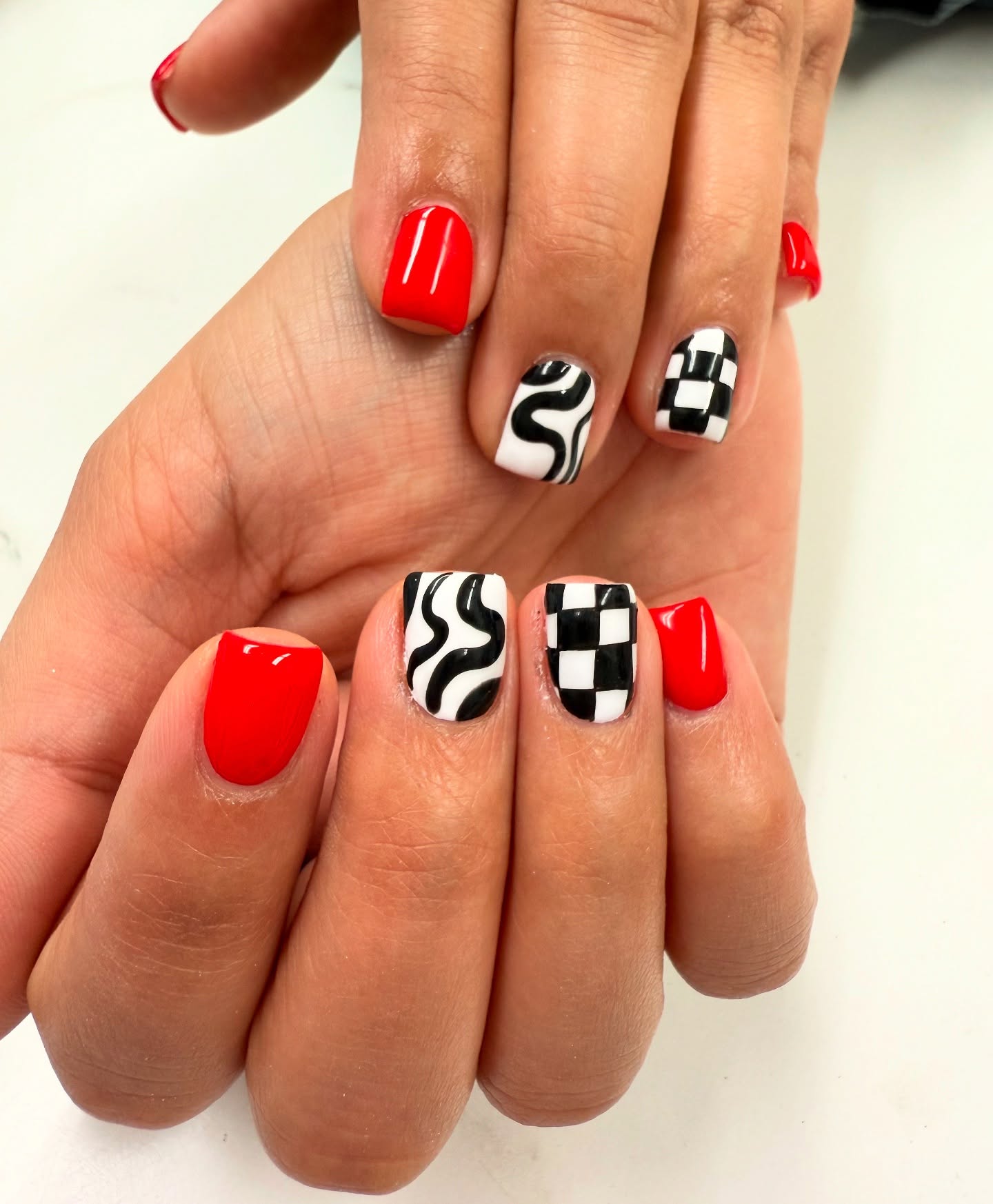Short square nails mixing solid red with black-and-white wavy checker and swirl patterned accent nails
