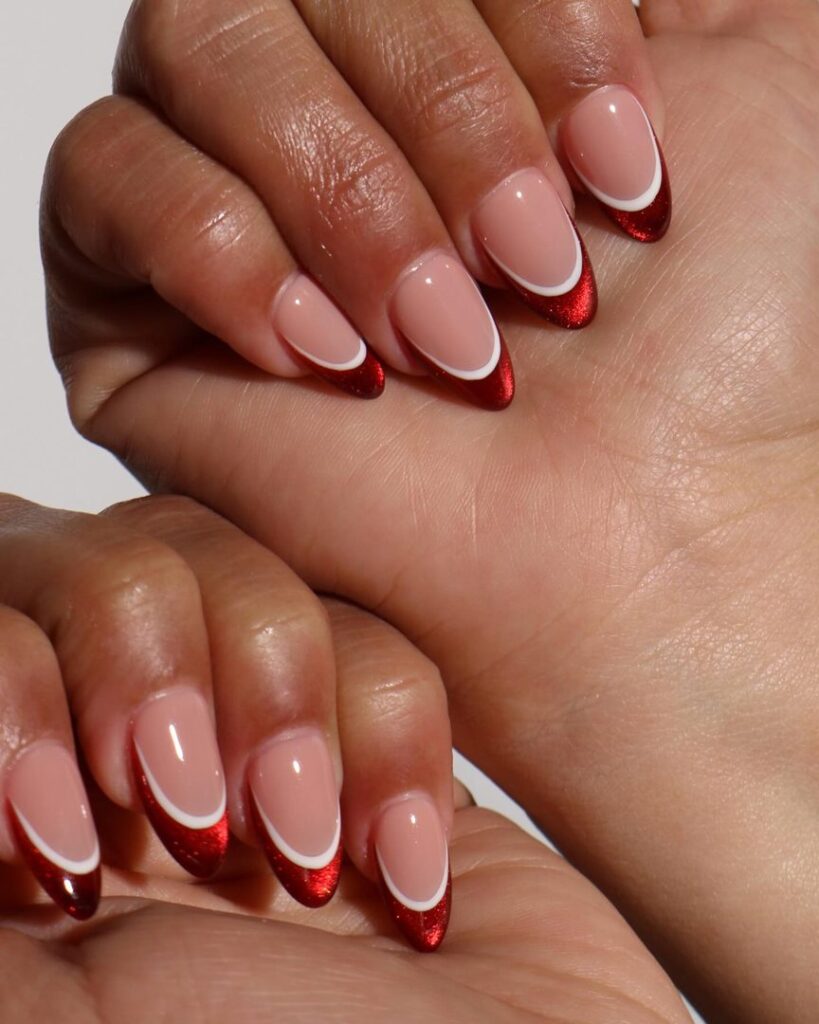 Medium oval nails with red metallic glitter tips and a fine white inner tip arc on a sheer nude base