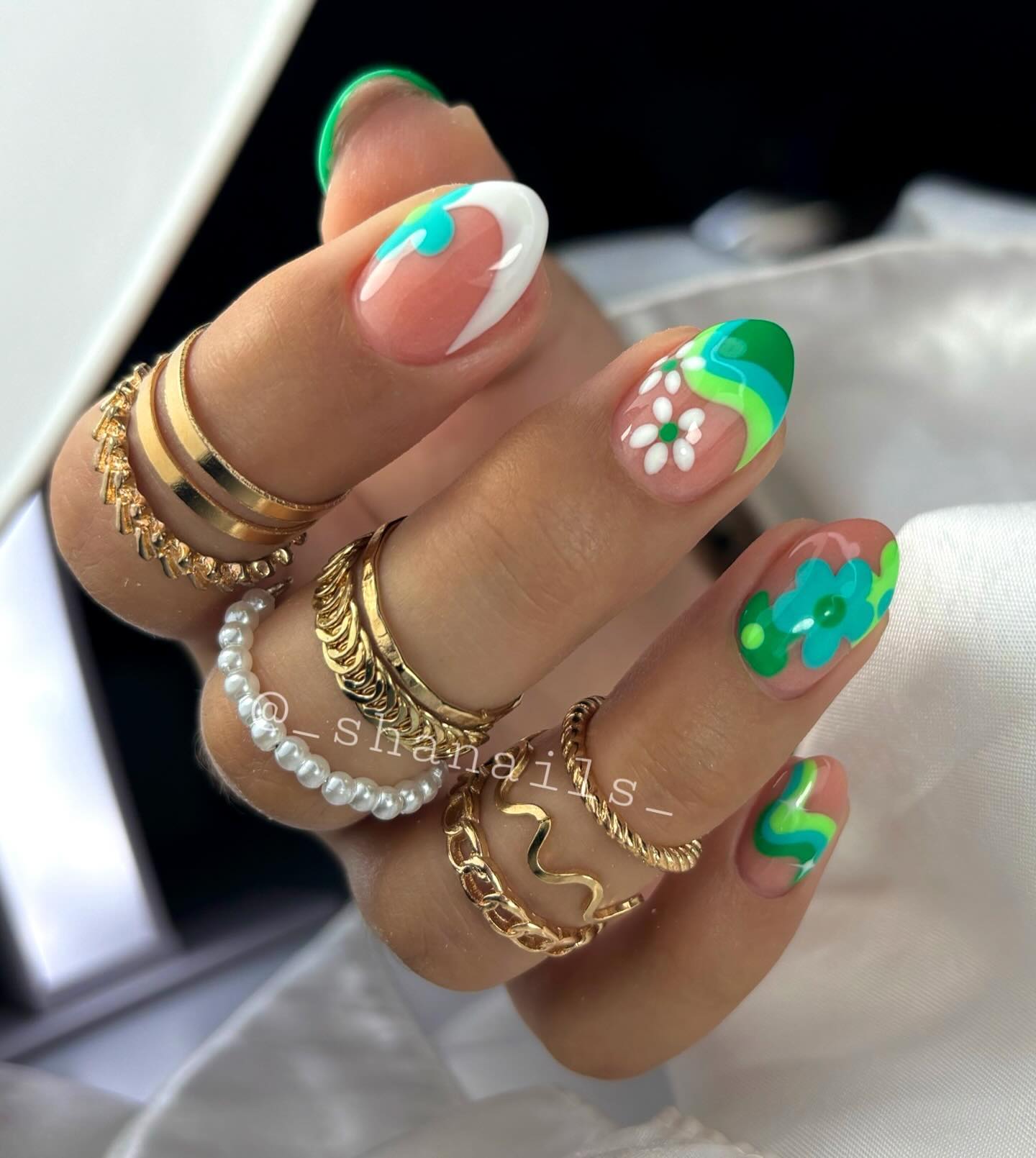 Short almond nails featuring swirling green and teal retro waves, white daisy, and bold teal floral on nude base