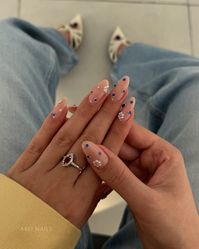 nails decorated with tiny blue rhinestones and white pearl flower accents