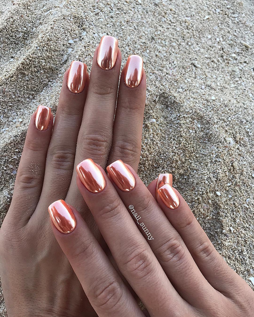 Lustrous rose gold chrome mirror-finish nails shot on sand