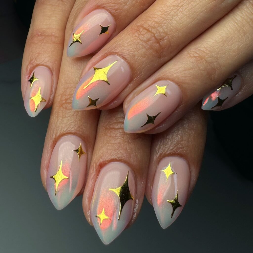 Almond nails with a sheer peach and teal aurora ombre base and 3D gold star charms