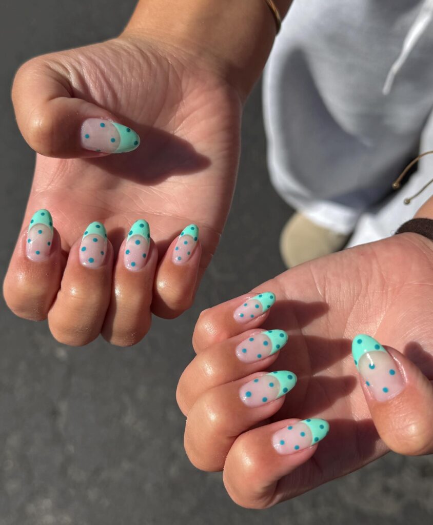 Sheer nude almond nails with mint green tips and scattered turquoise polka dots on both hands