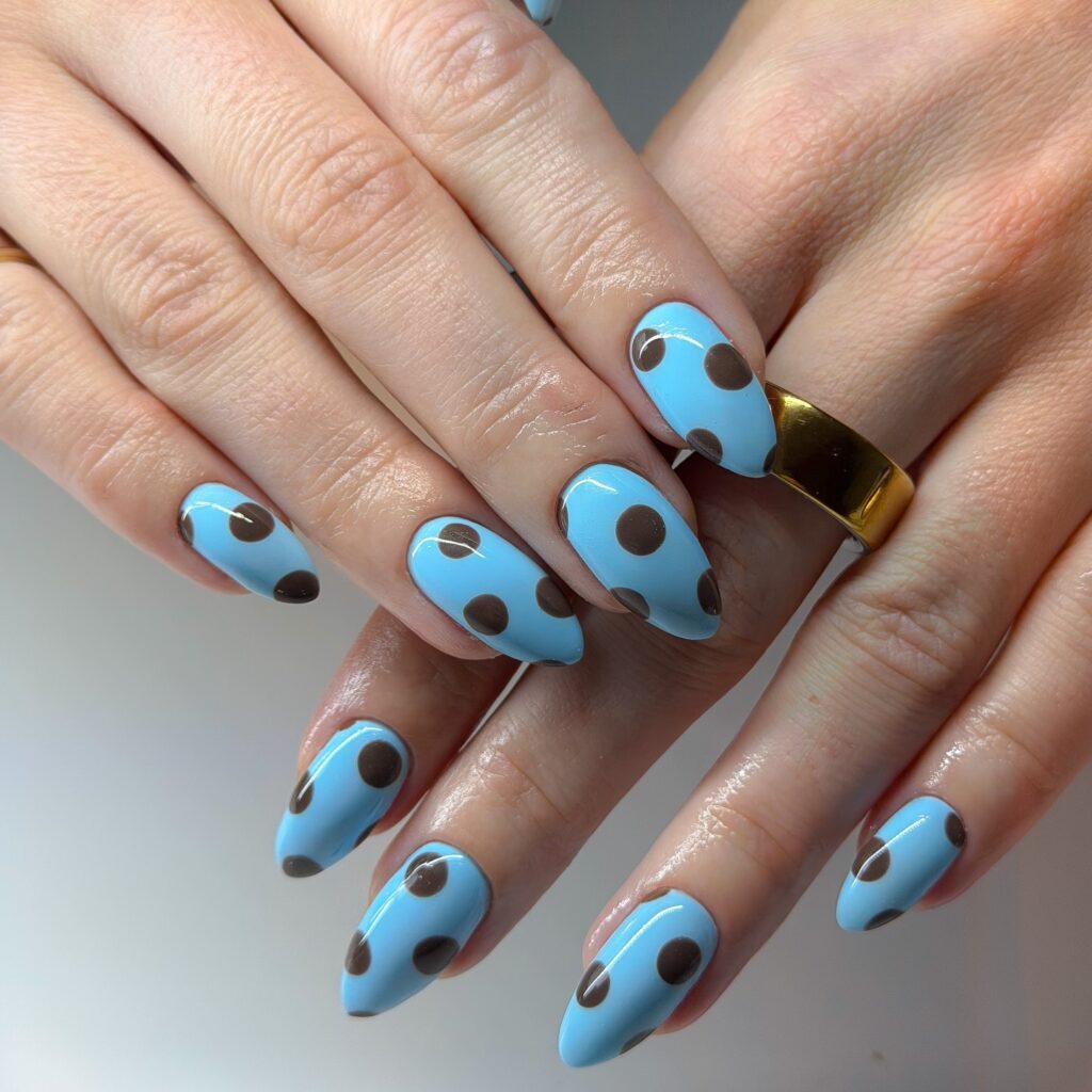 Almond nails in bright sky blue with large round chocolate brown polka dots in a bold, graphic retro pattern