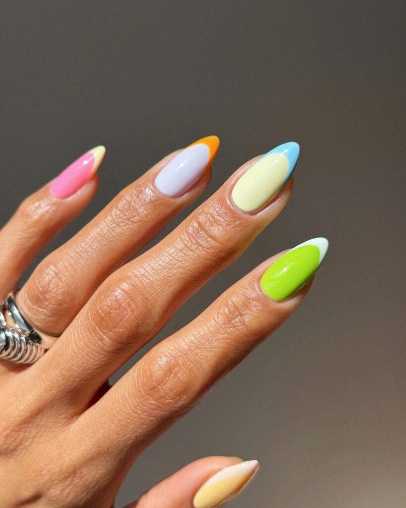 Medium oval nails each with a different bold tip — orange, pink, lavender, yellow-green, and lime — on a sheer nude base