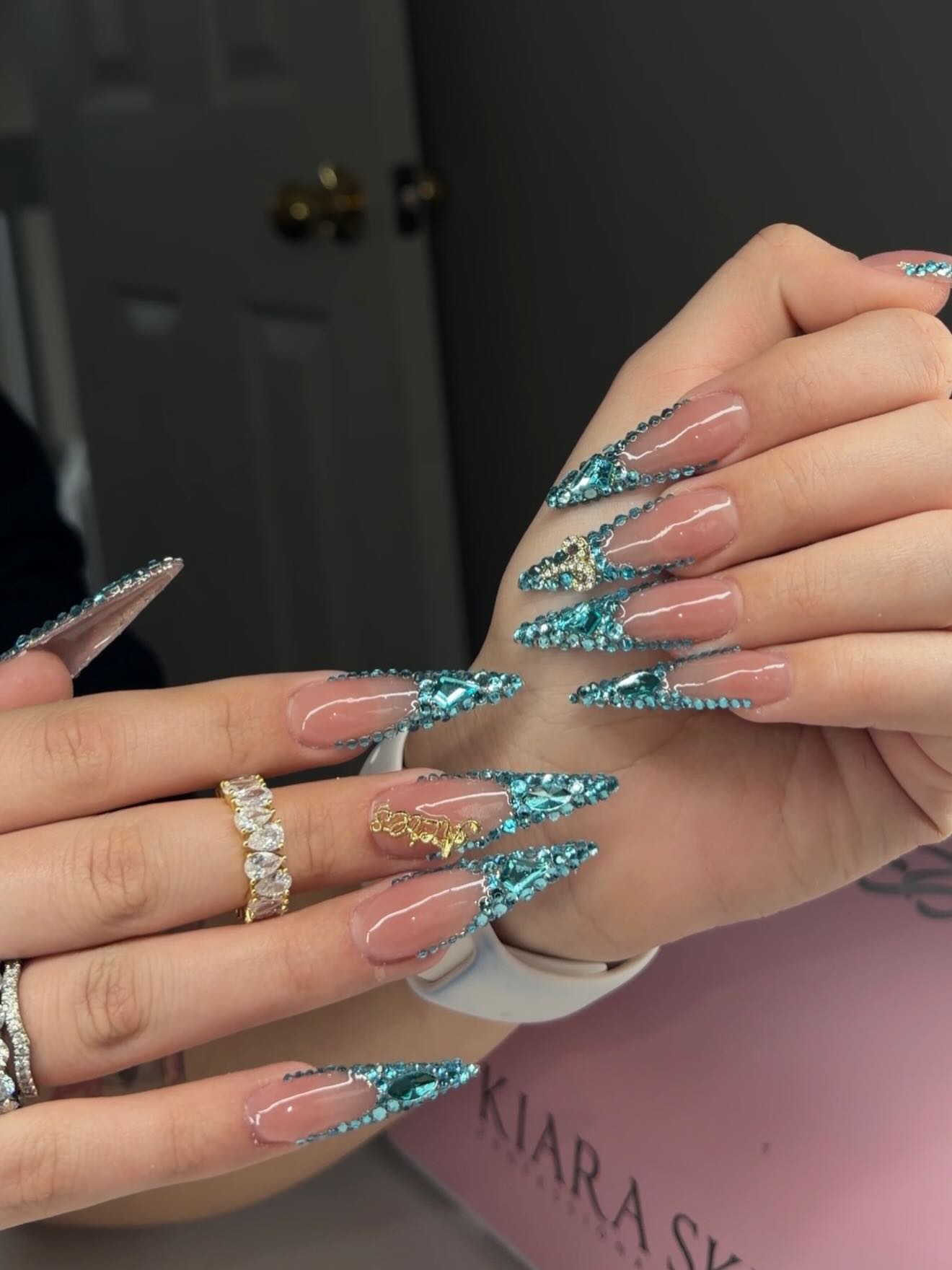 Extra long stiletto nails with dramatic teal rhinestone lightning bolt designs on a nude base