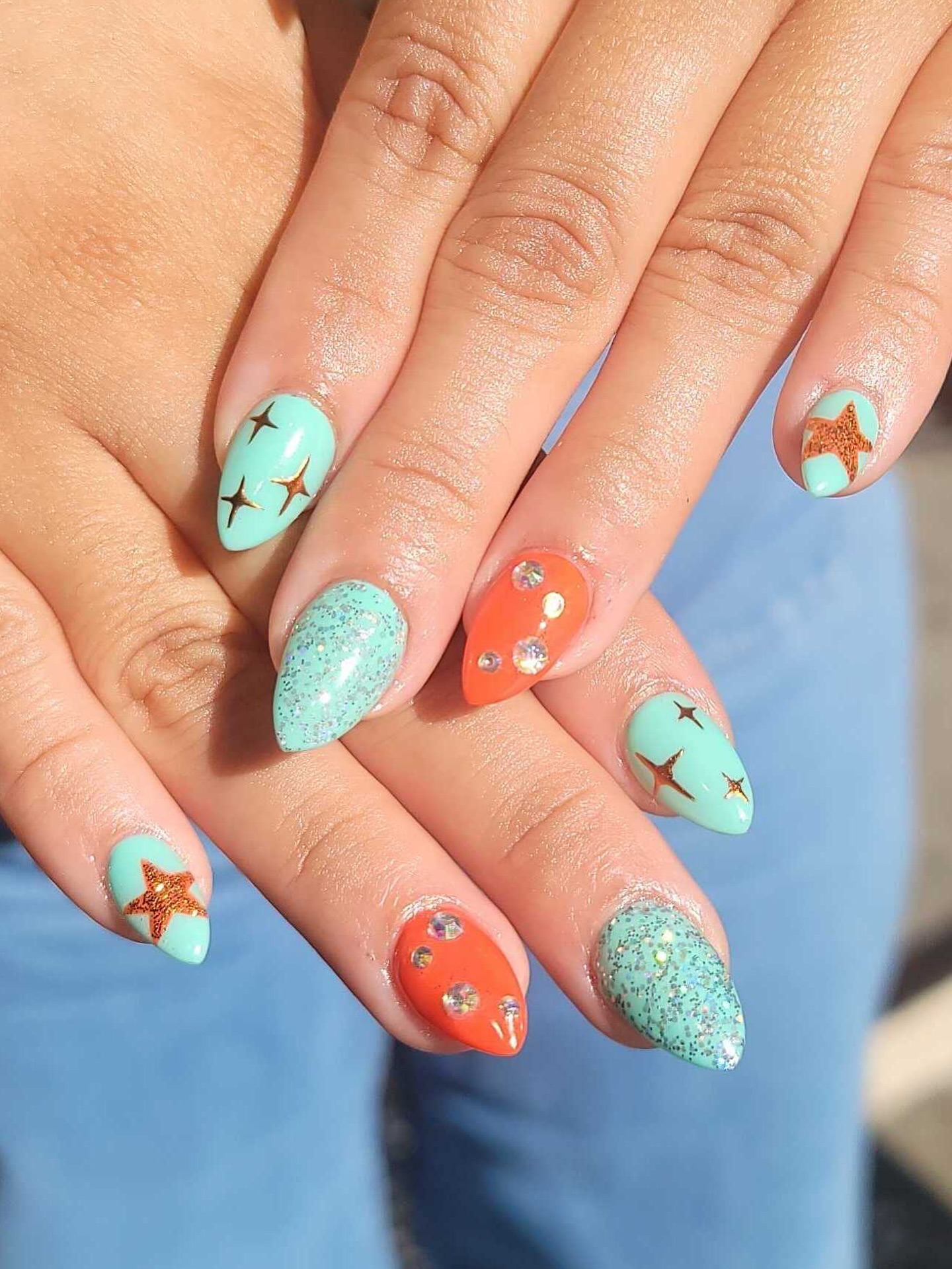 Mint green and orange almond nails with gold starfish accents and crystal rhinestones