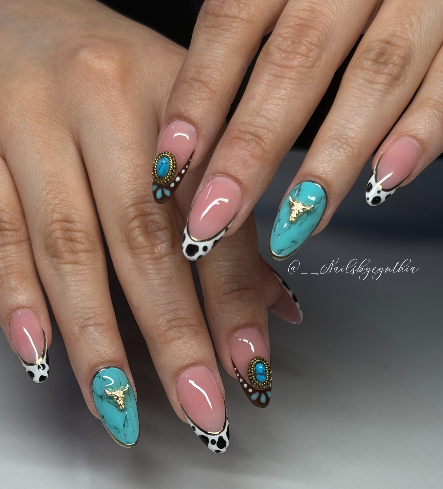 Long almond nails with full turquoise stone nail featuring gold longhorn charm, cow print French tips, and bronze sunburst detail