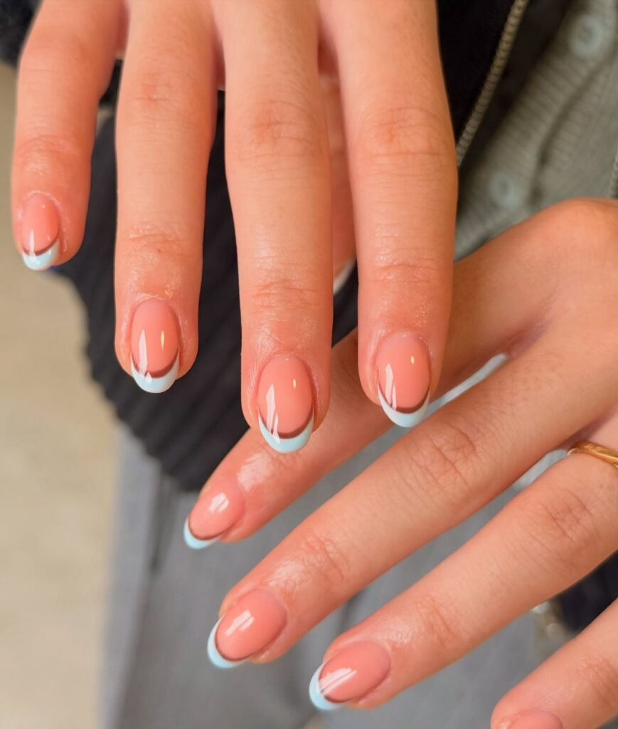 Glossy round nails with a nude base featuring a double French tip lined in dark brown and baby blue