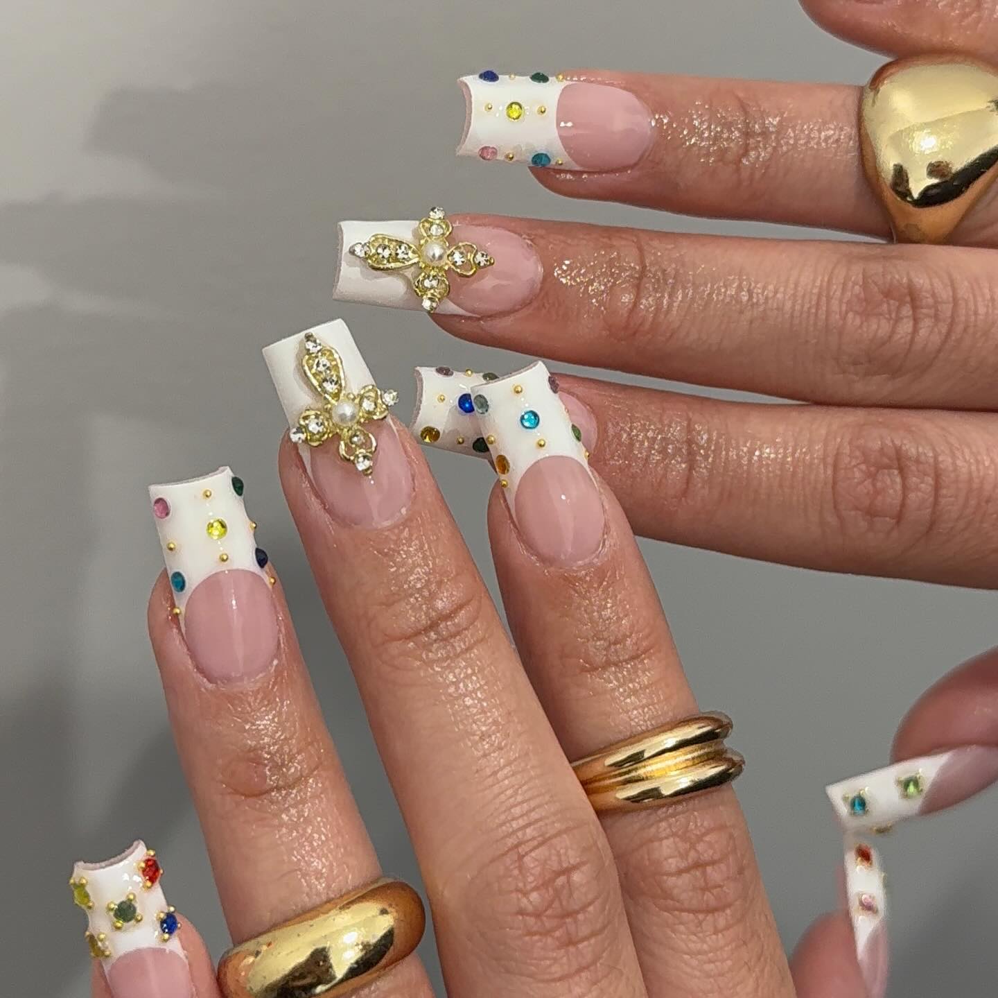 Square white French tip nails studded with multicolour rhinestones and a gold cross charm