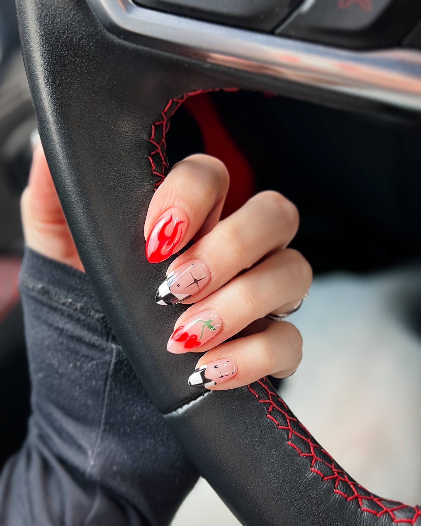 Eclectic almond nails featuring a red flame, black-and-white checkerboard tips, and a cherry accent on a sheer base