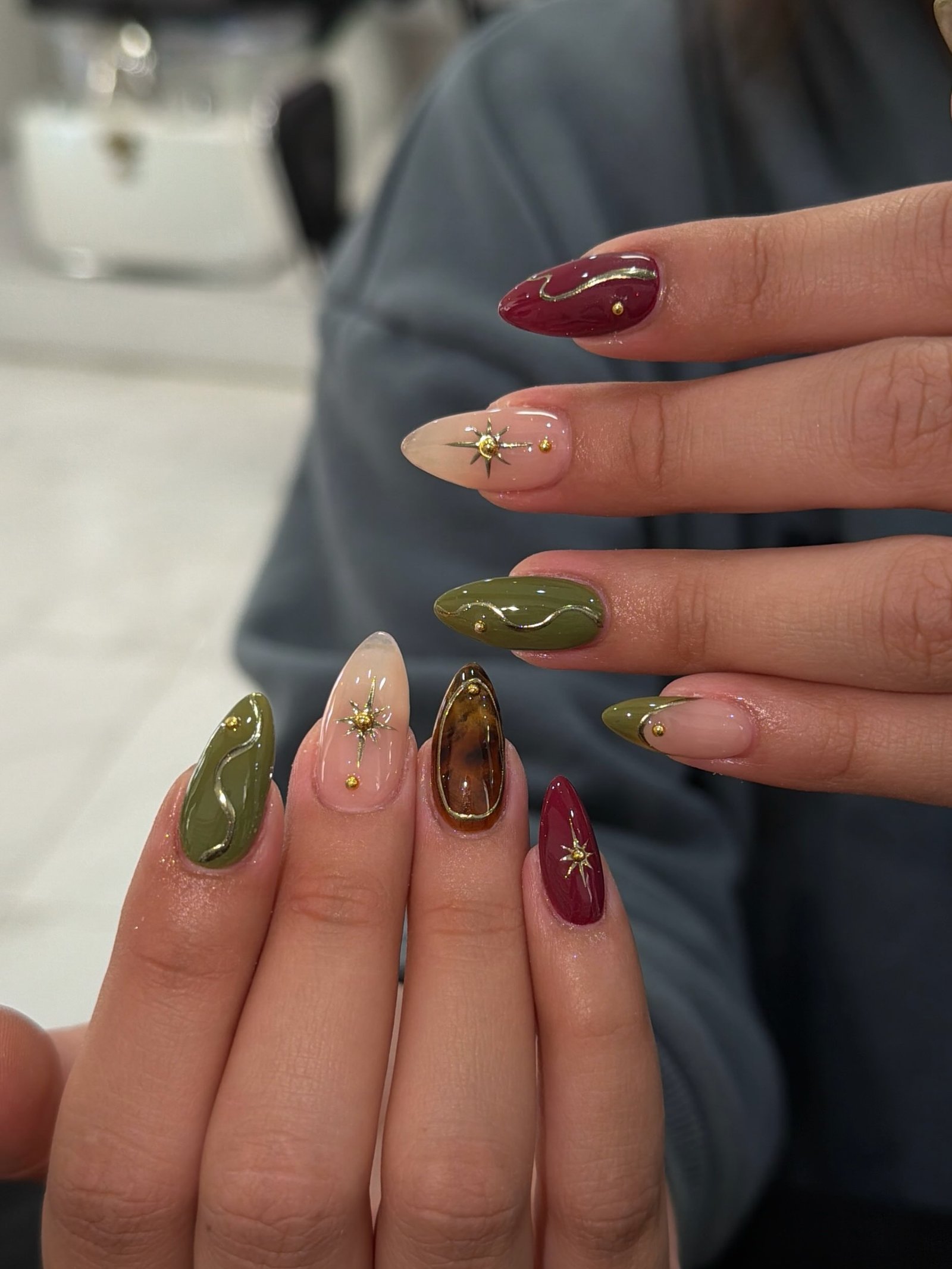 Deep burgundy and olive green almond nails with delicate gold accents