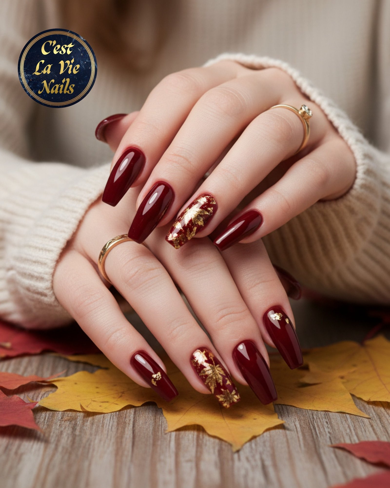 Deep burgundy almond nails with gold-toned accents