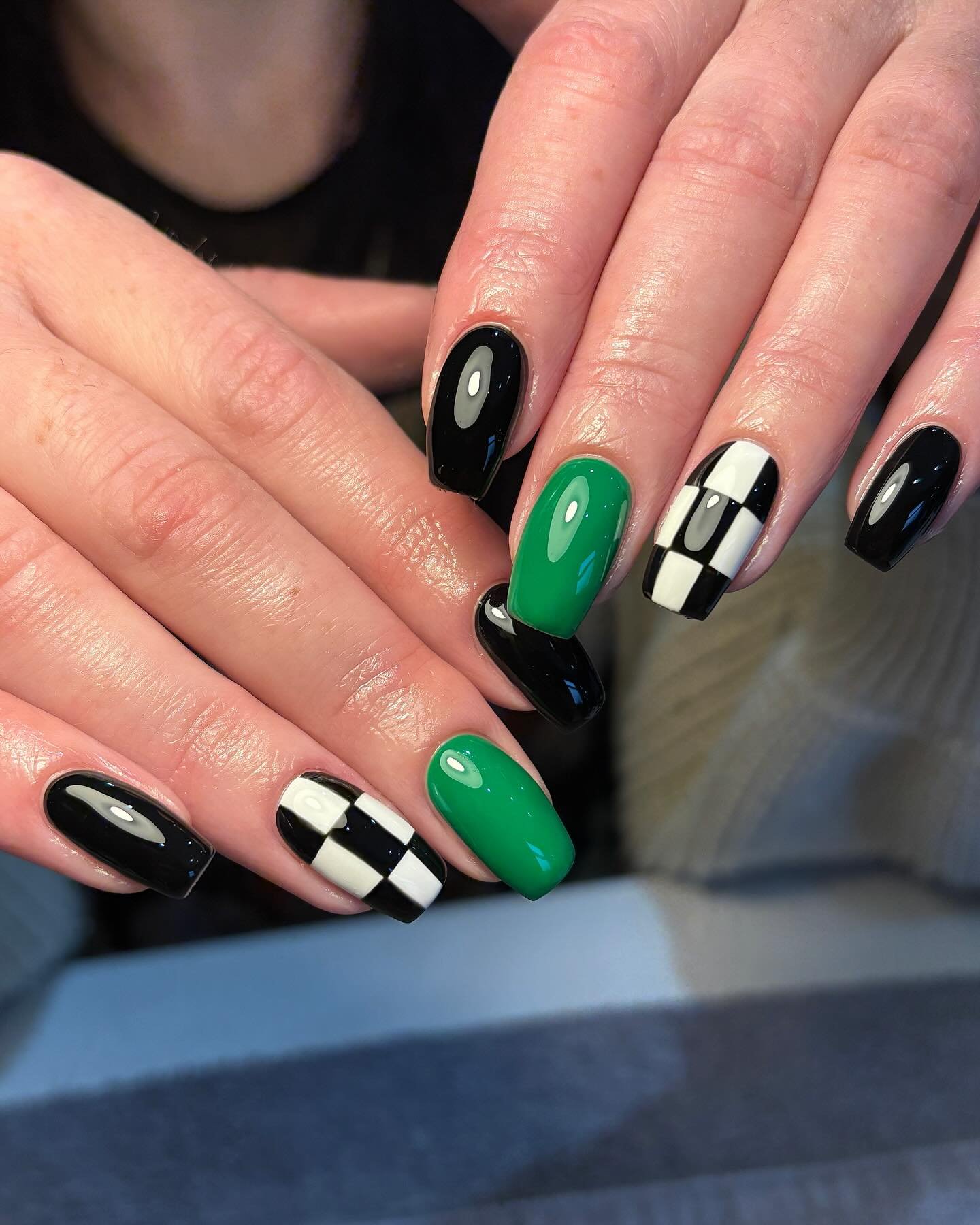 Black almond-shaped nails feature alternating green accents and small white linear details