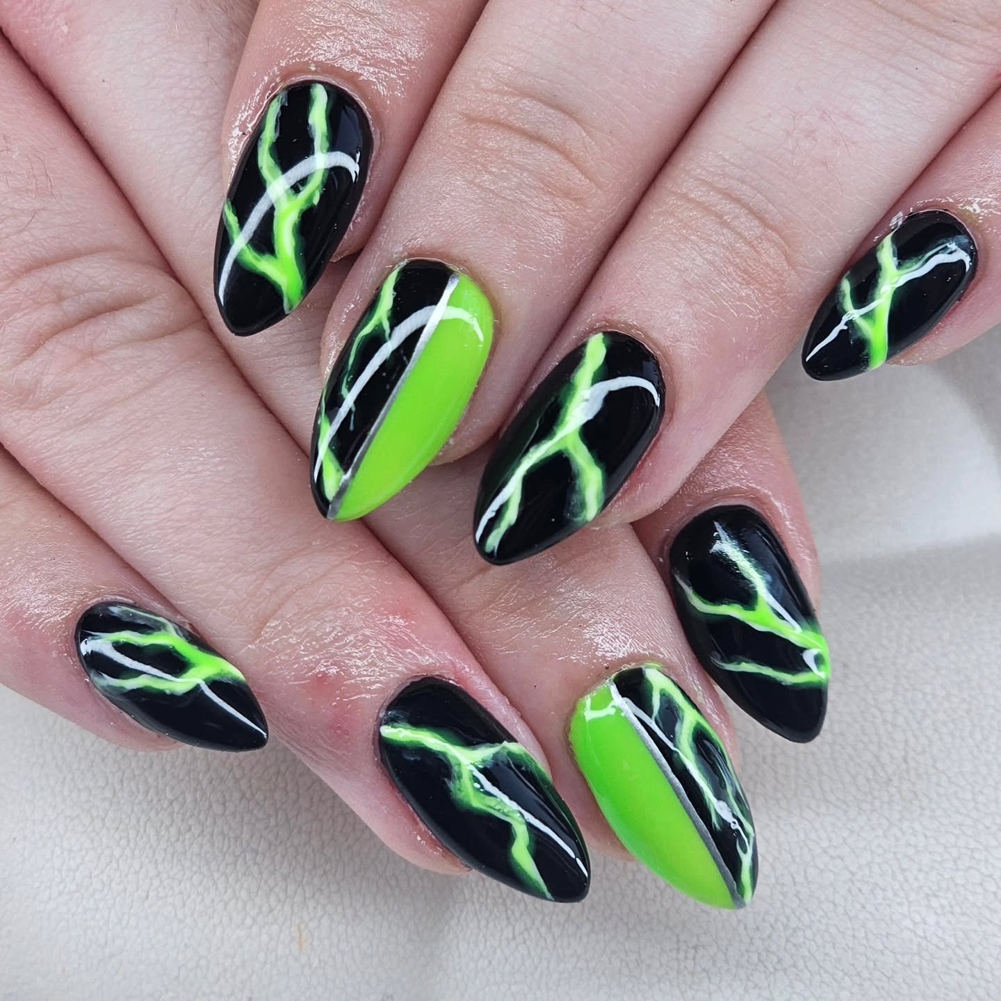 Almond nails combine neon green and black bases with thin, sweeping light-green and white abstract lines