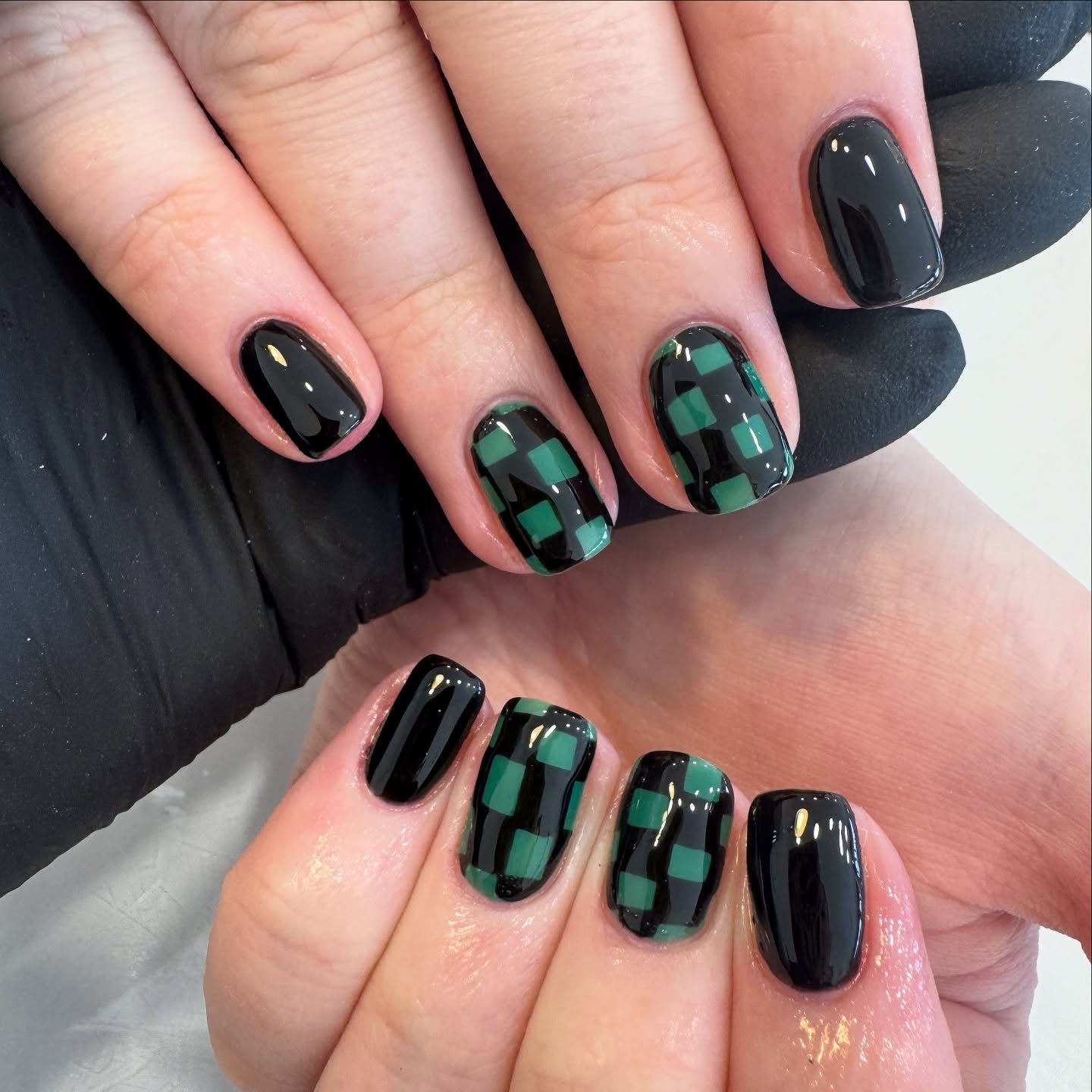 Short rounded-square nails combine glossy black with green-and-black checkered accent panels