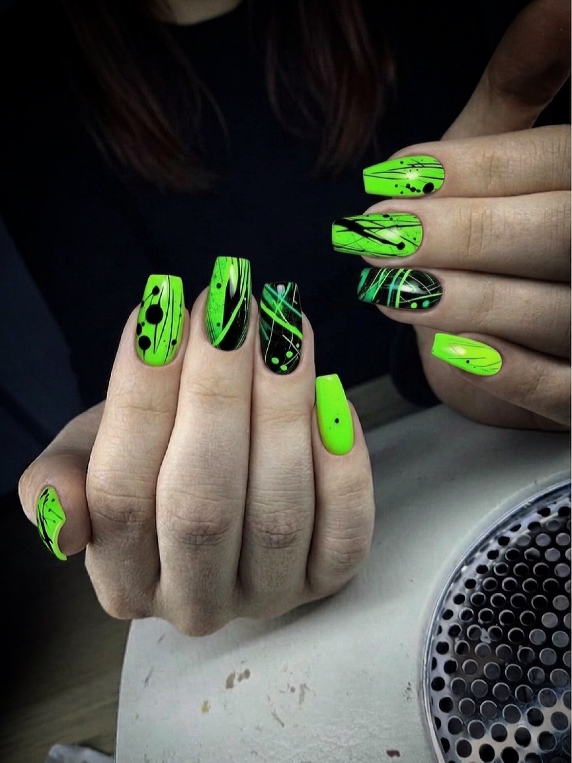 Long nails combine vivid neon green and black with bold graphic patterns and outlined accents