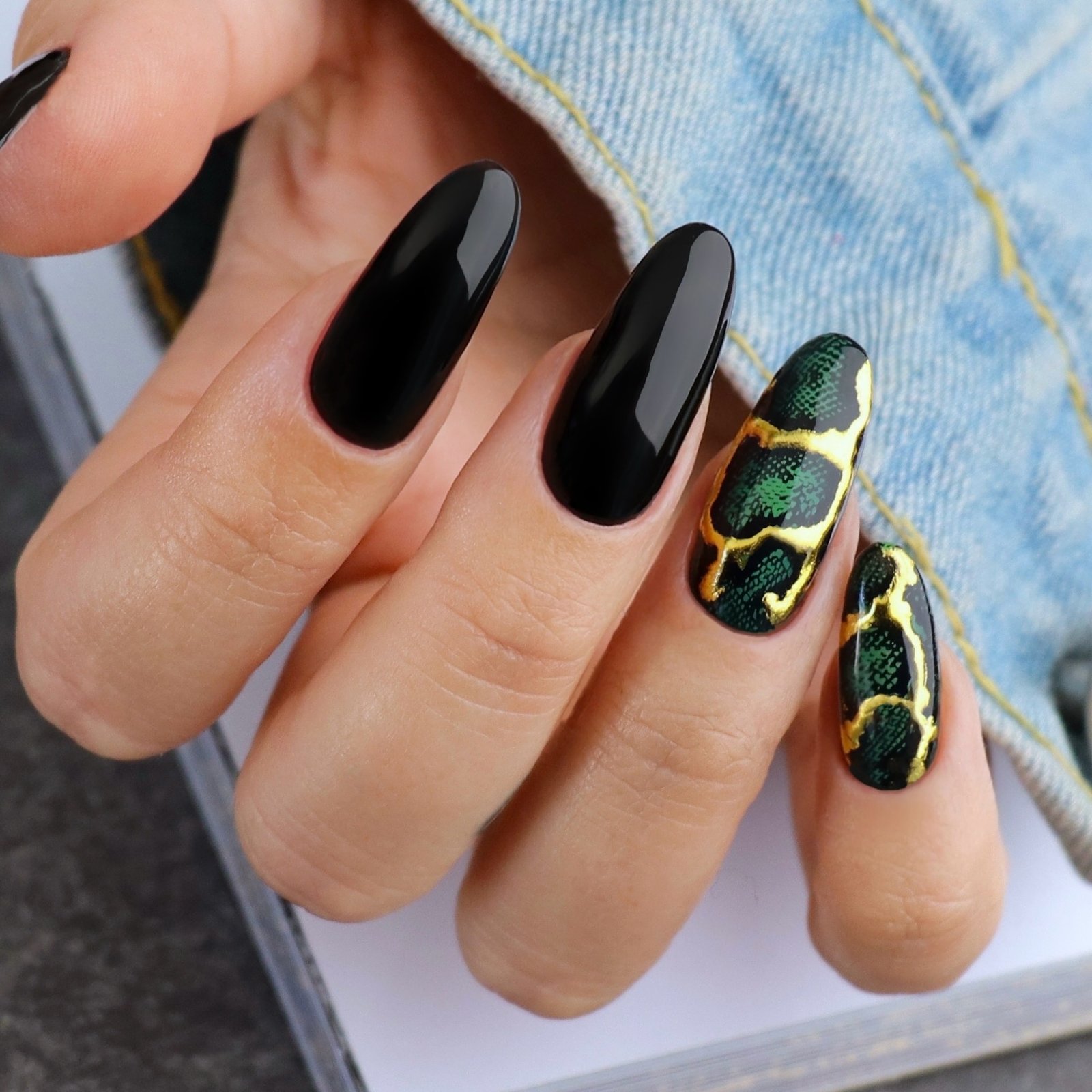 Long nails combine black, green, and plaid sections with small gold-toned accent details