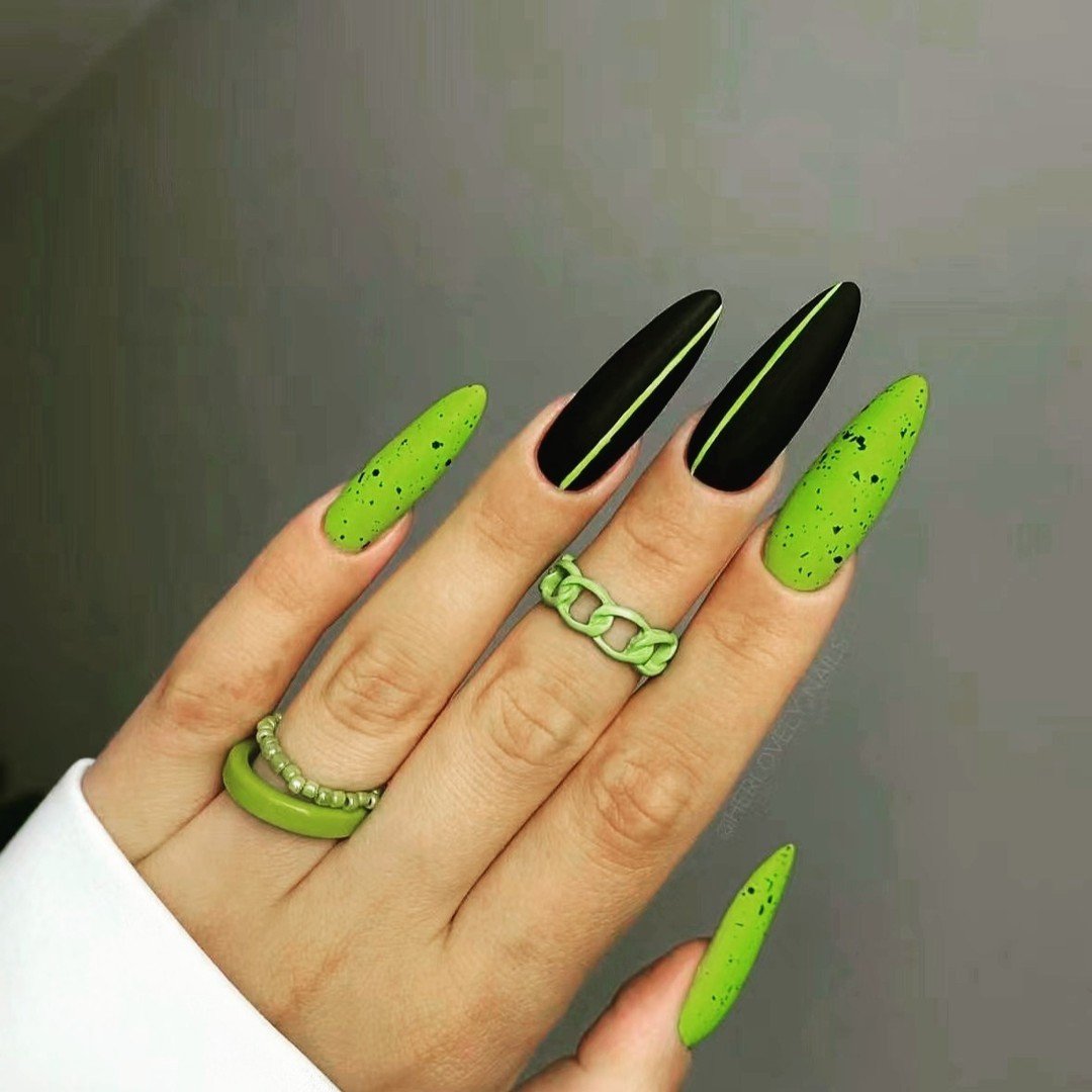 Long stiletto nails combine neon green and black with tiny dark dot details on the green surfaces