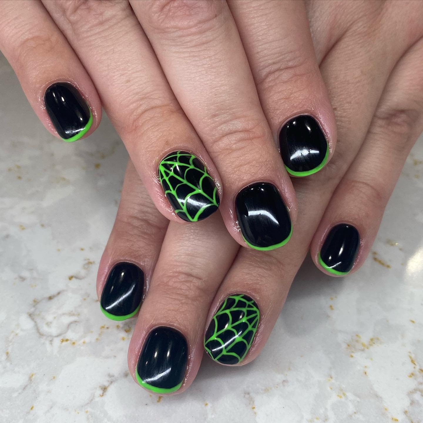 Short rounded nails are mostly glossy black, with selected nails decorated by bright green web-like line patterns