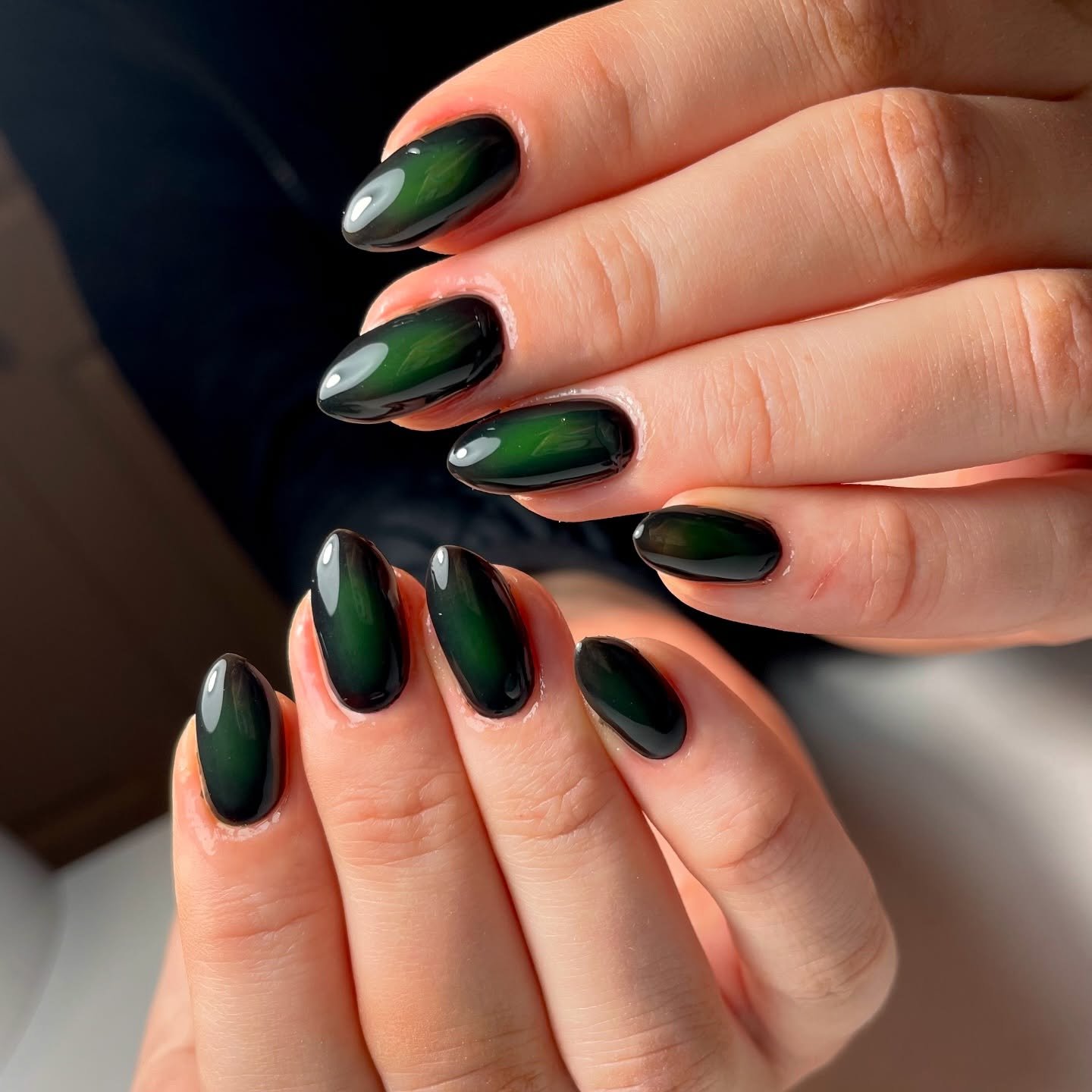 Medium-length almond nails blend deep green and black in a glossy, softly graduated finish