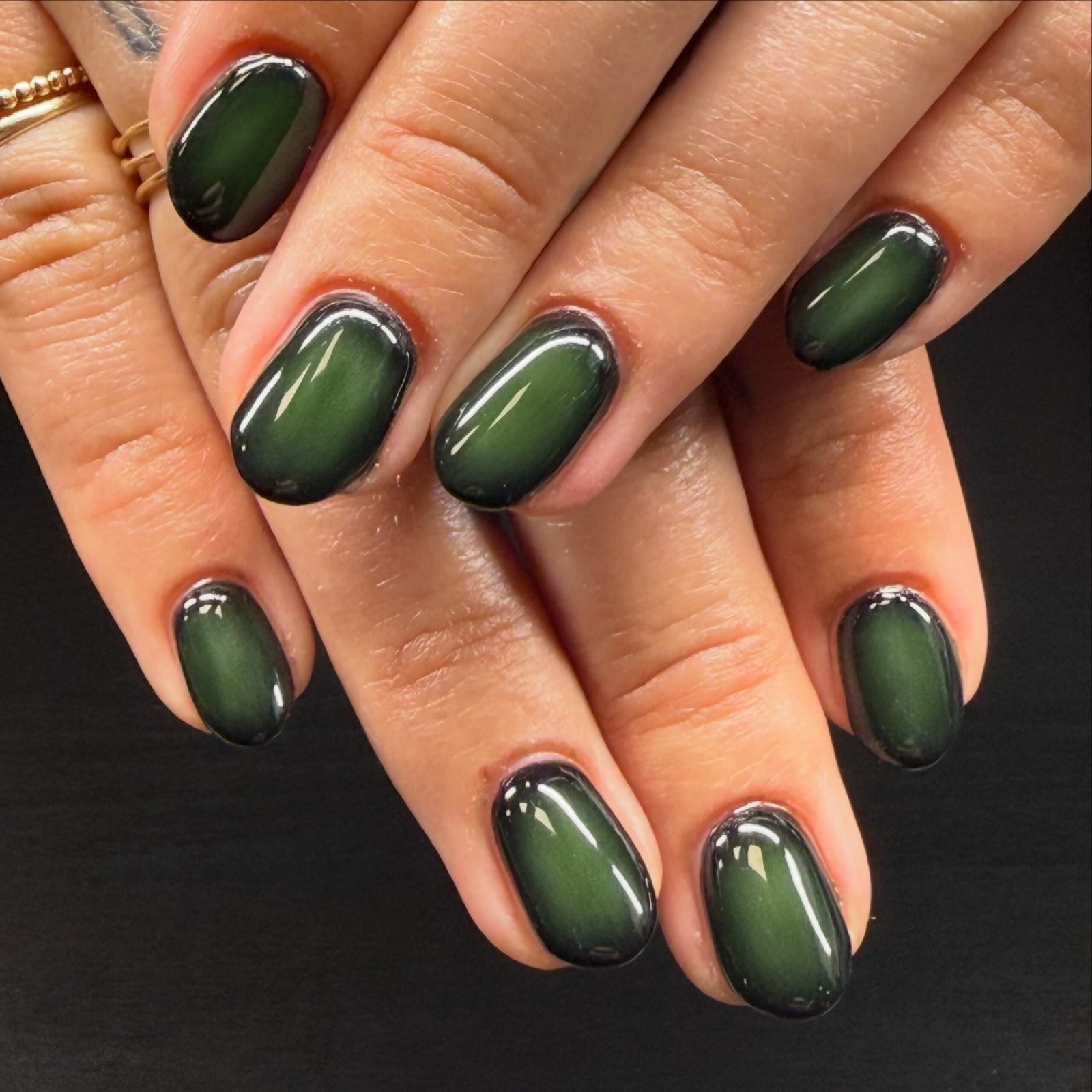 Short rounded nails are coated in a uniform glossy dark green shade