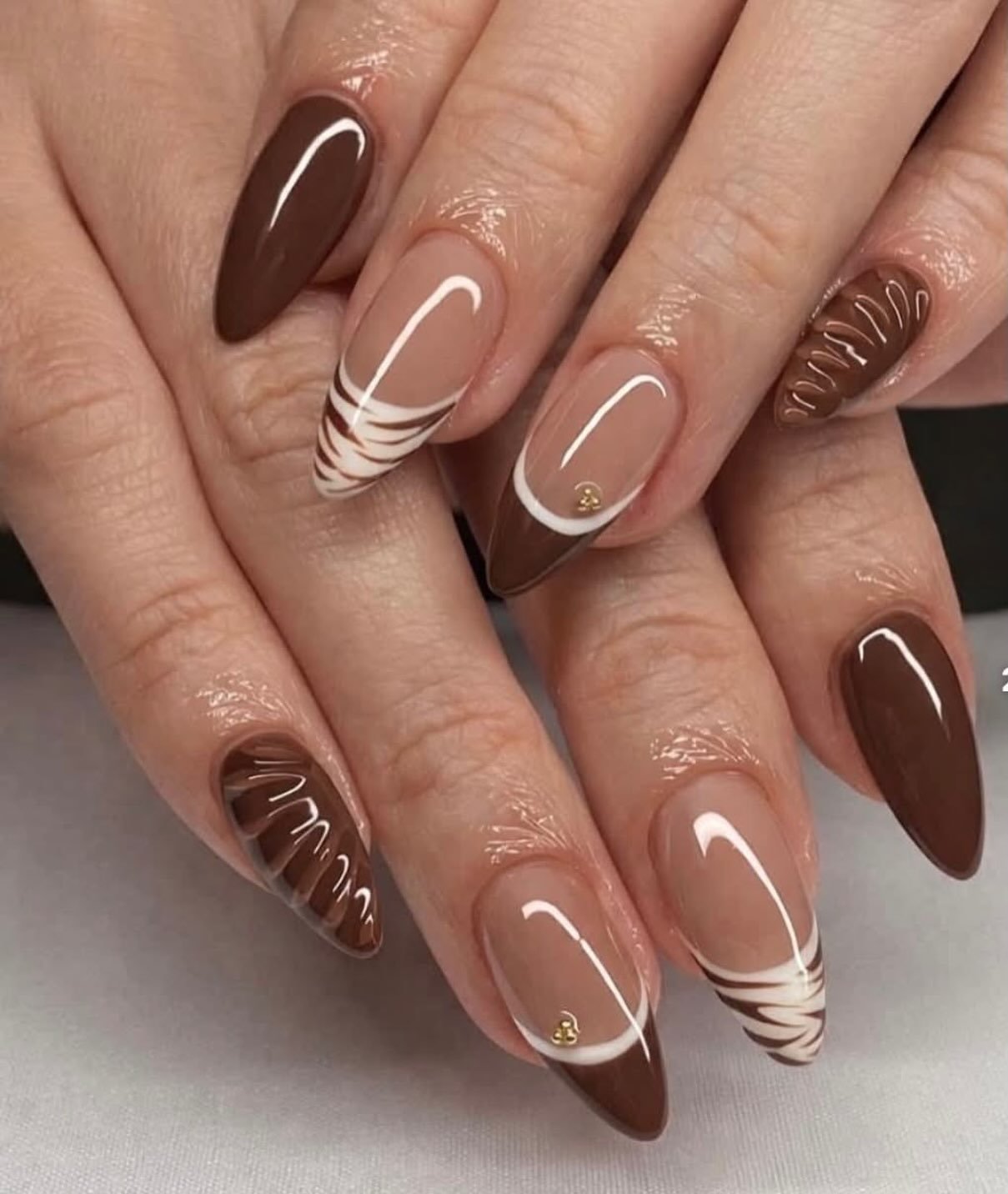 Long almond nails alternate solid chocolate brown, nude bases with curved white French lines, and a tortoiseshell-style accent.