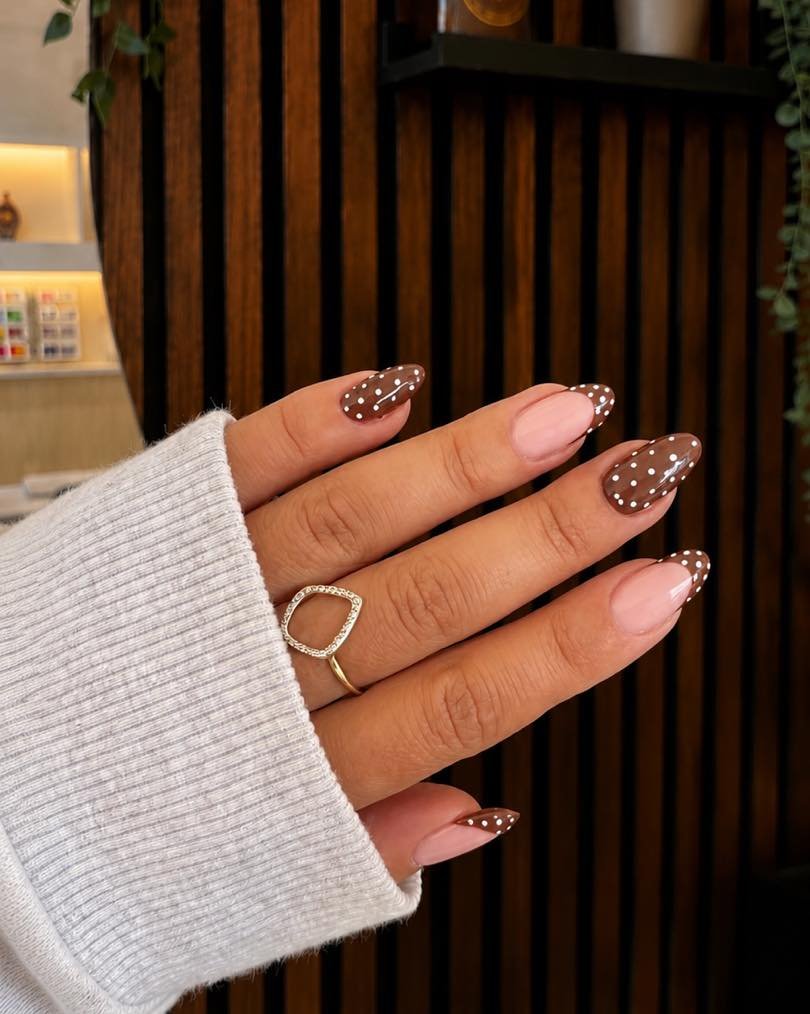 Long almond nails pair a pale pink base with chocolate-brown tips, with sparkling dotted details decorating several accent nails.
