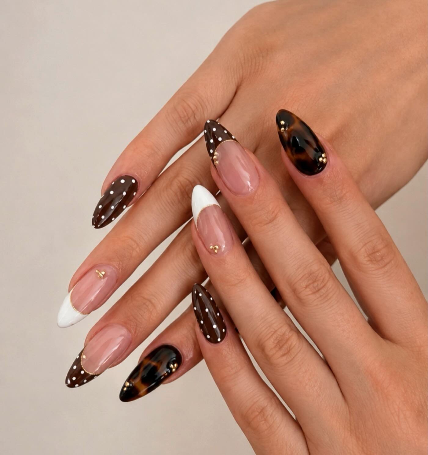 Long pointed nails combine blush pink with chocolate-brown and patterned dark tips, plus small sparkling accents.
