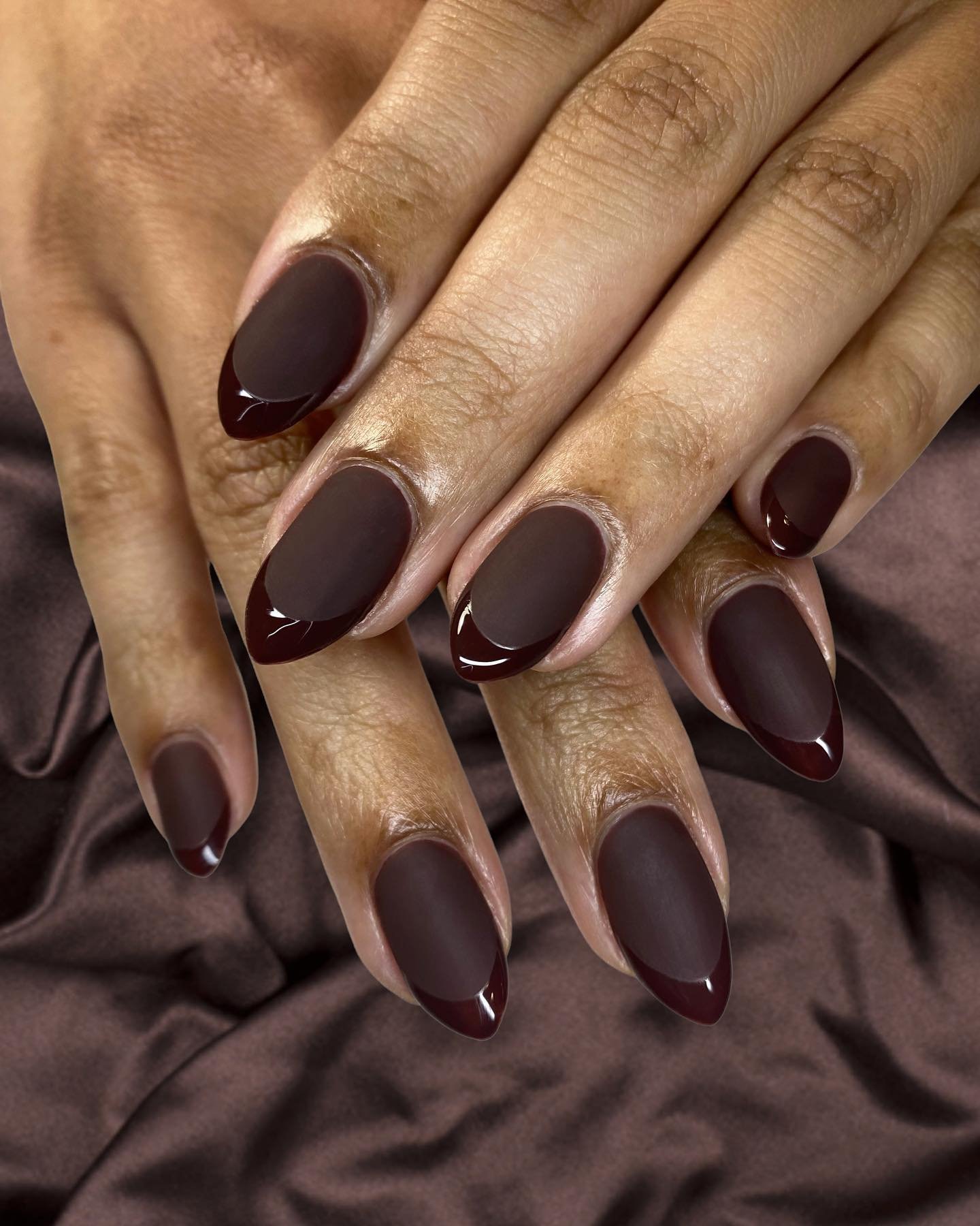 Long almond nails are covered in a uniform deep chocolate-brown polish with a glossy finish.