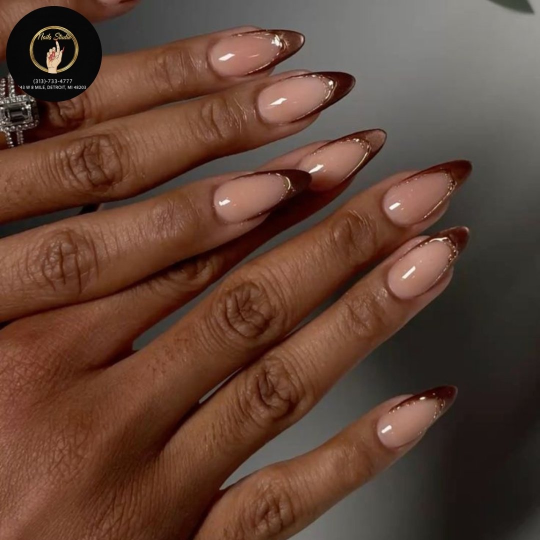 Long almond nails feature a nude-pink base with slim chocolate-brown French tips for a clean contrast.