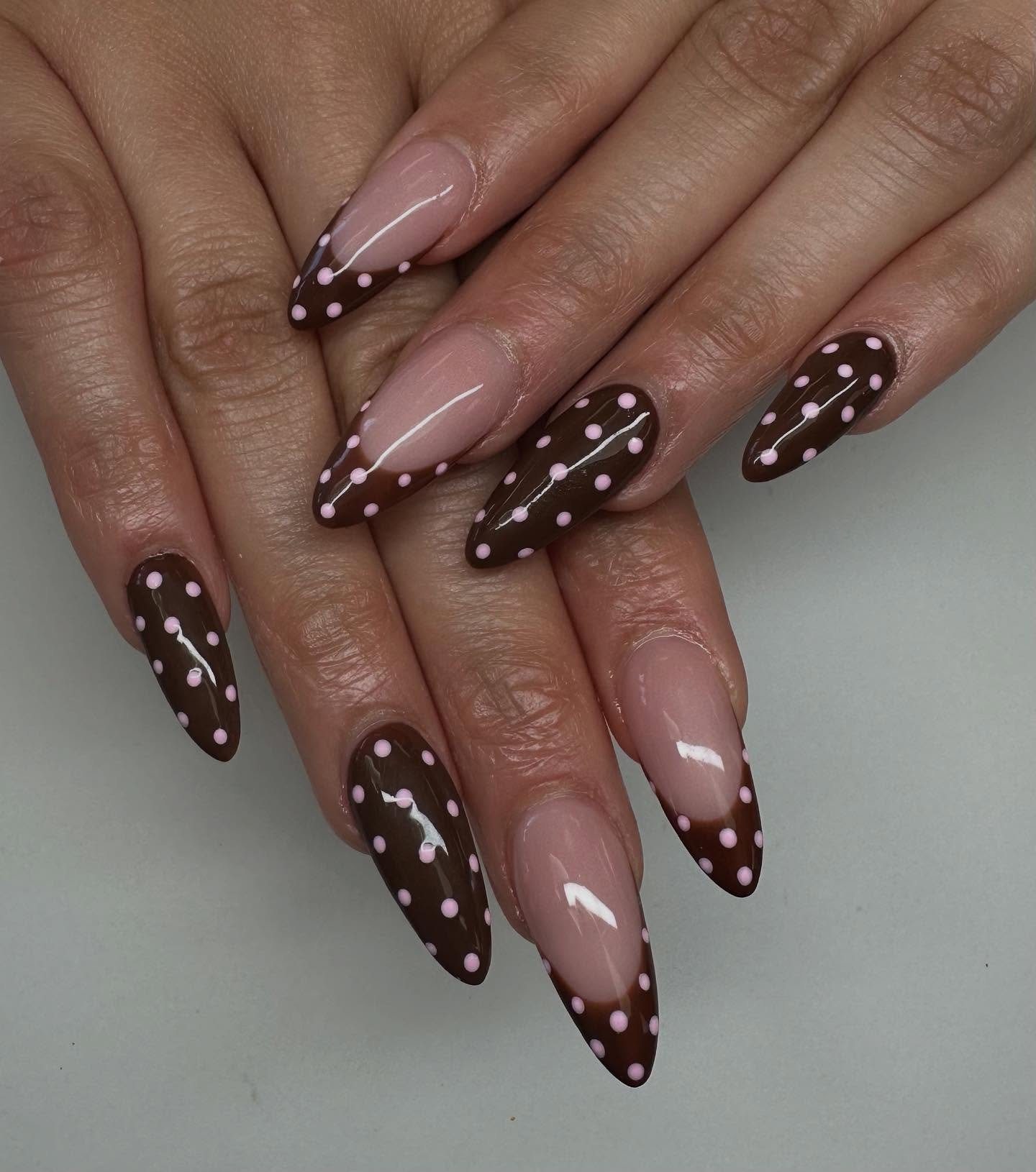 Long almond nails combine chocolate-brown French tips with small white dotted and floral-style accent details.
