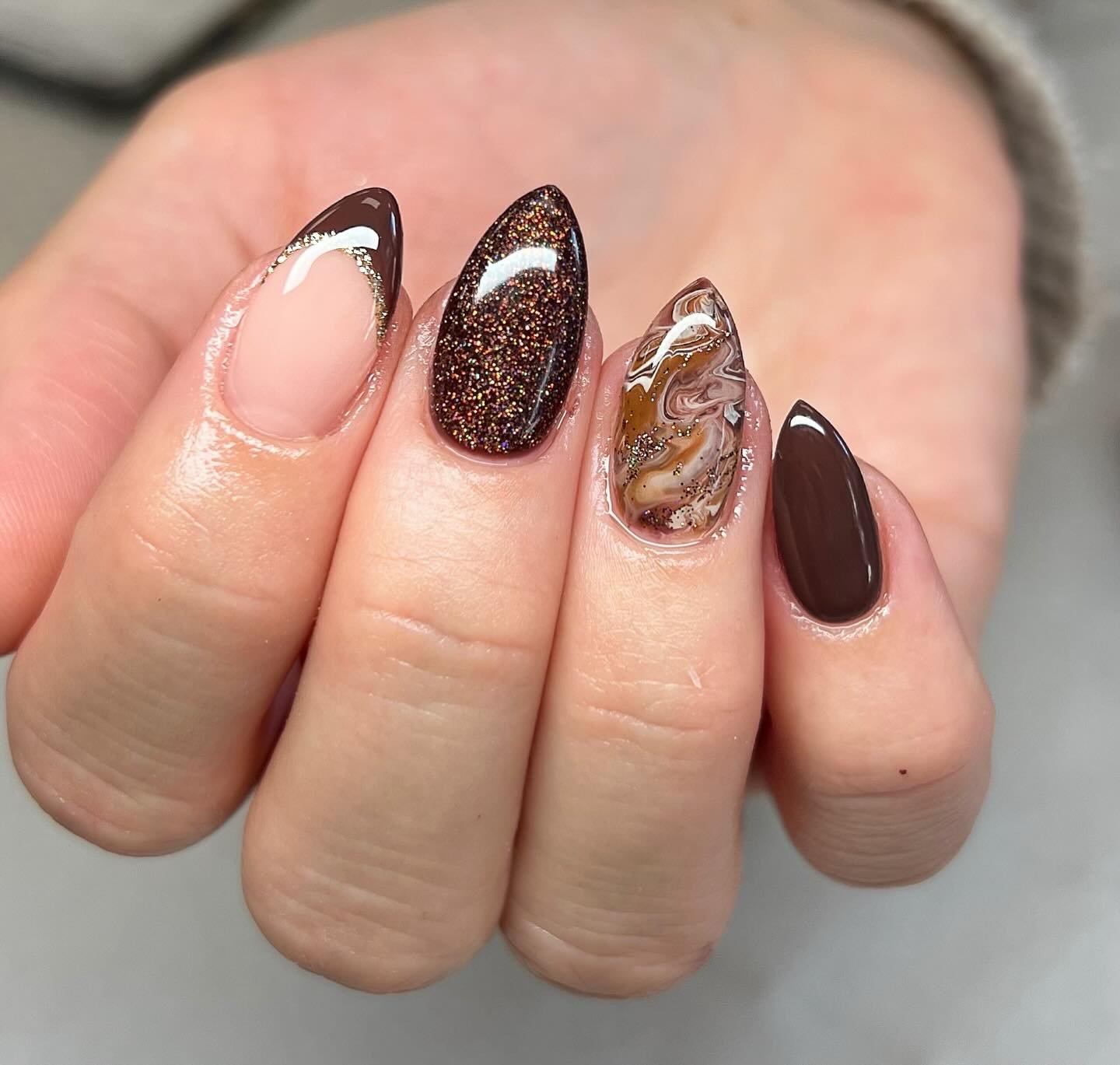 Short nails mix nude and chocolate French details with a glittery brown accent and tortoiseshell-style patterning.