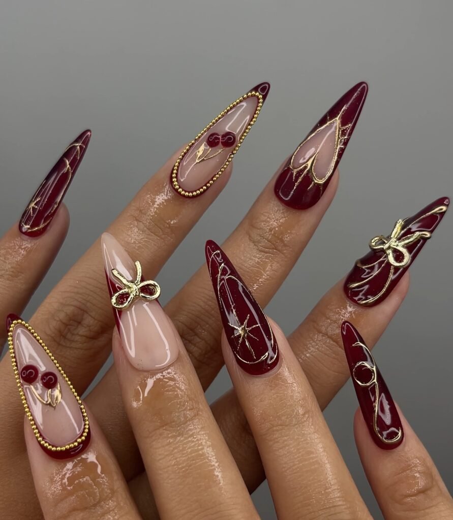 Long burgundy almond nails with gold bow and line accents