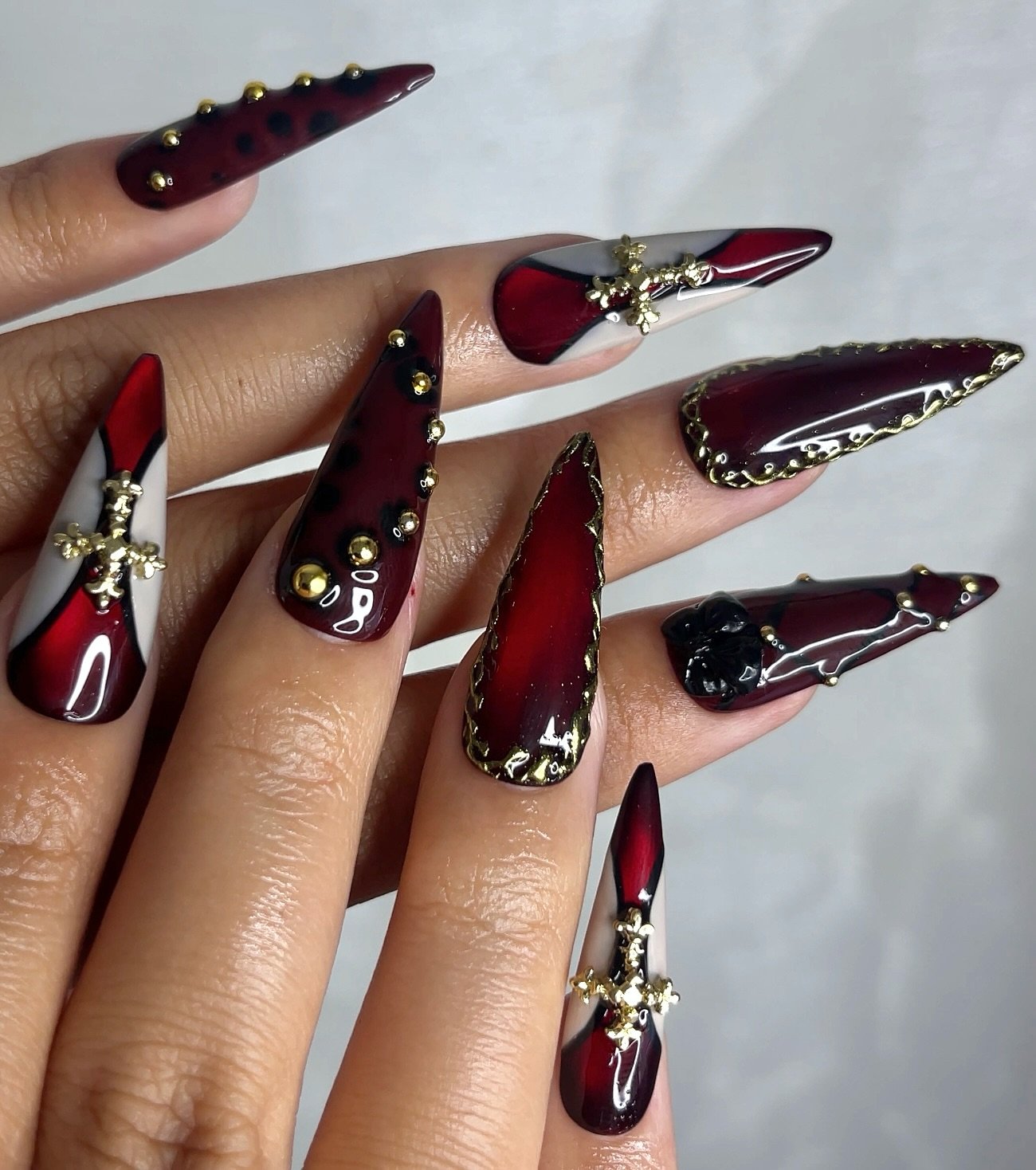 Deep burgundy stiletto nails with metallic embellished details