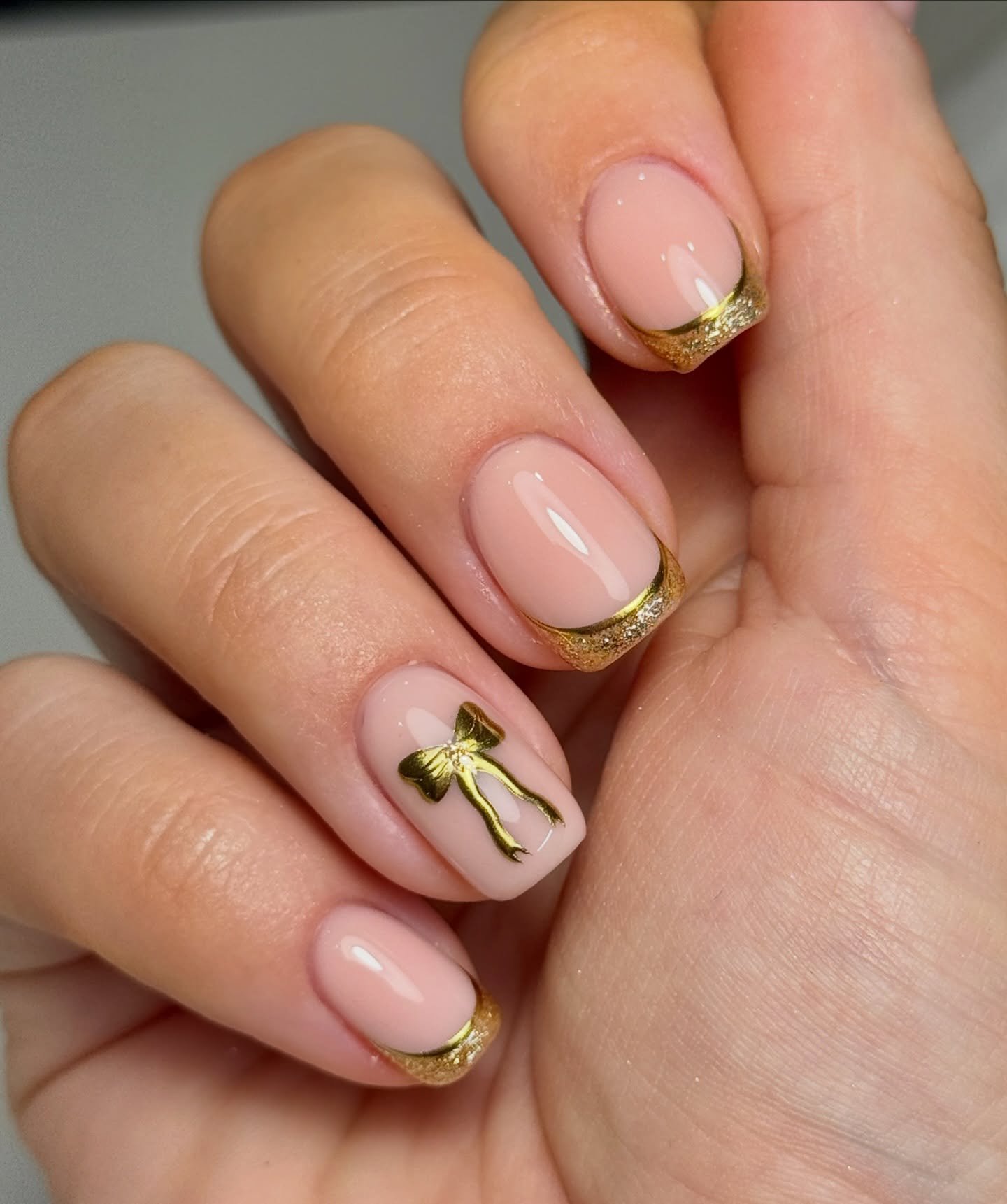 Nude Nails with Gold Glitter French Tips and Bow Accent