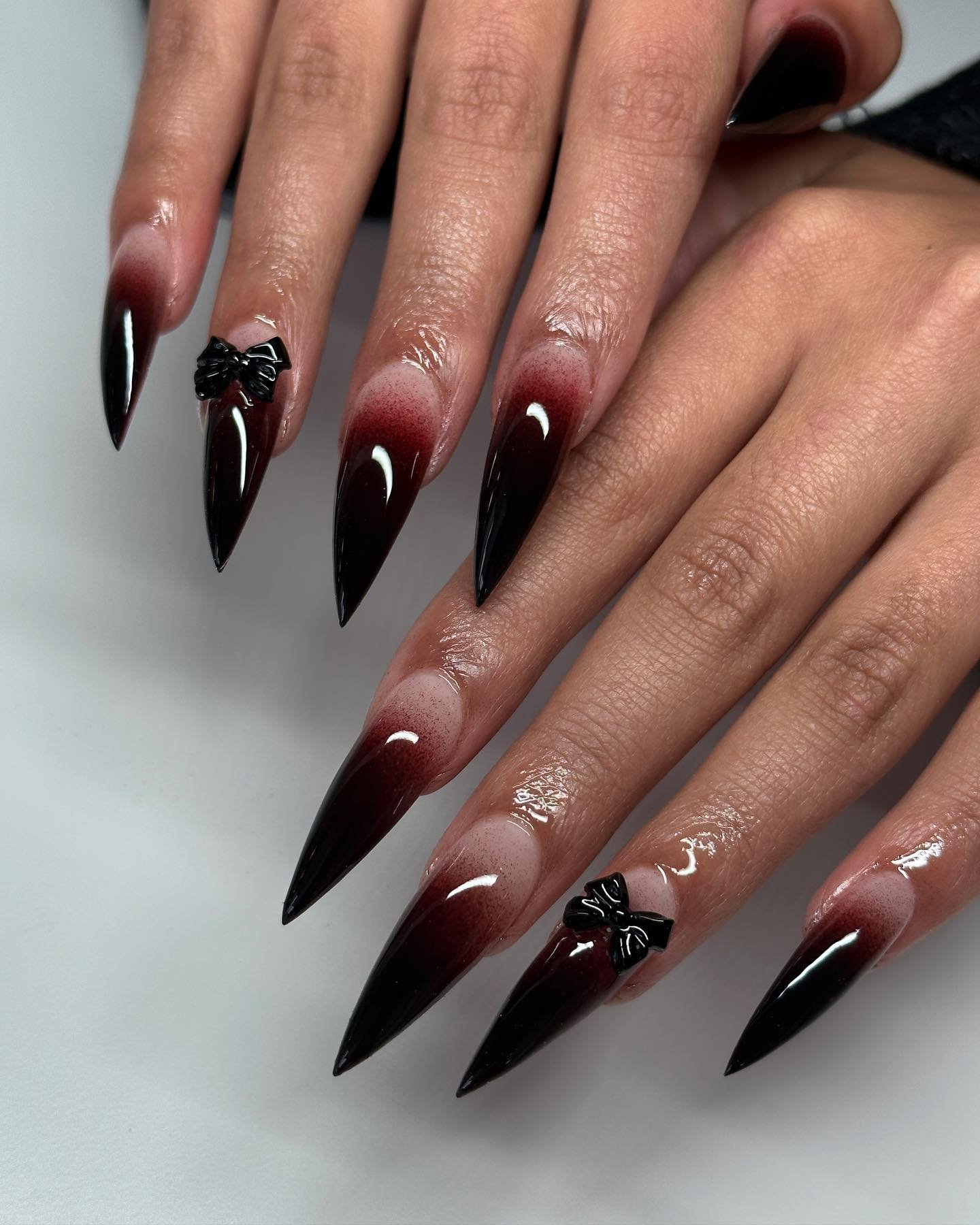 Black pointed stiletto nails feature dark red accents near the cuticle with small light details on a few nails.