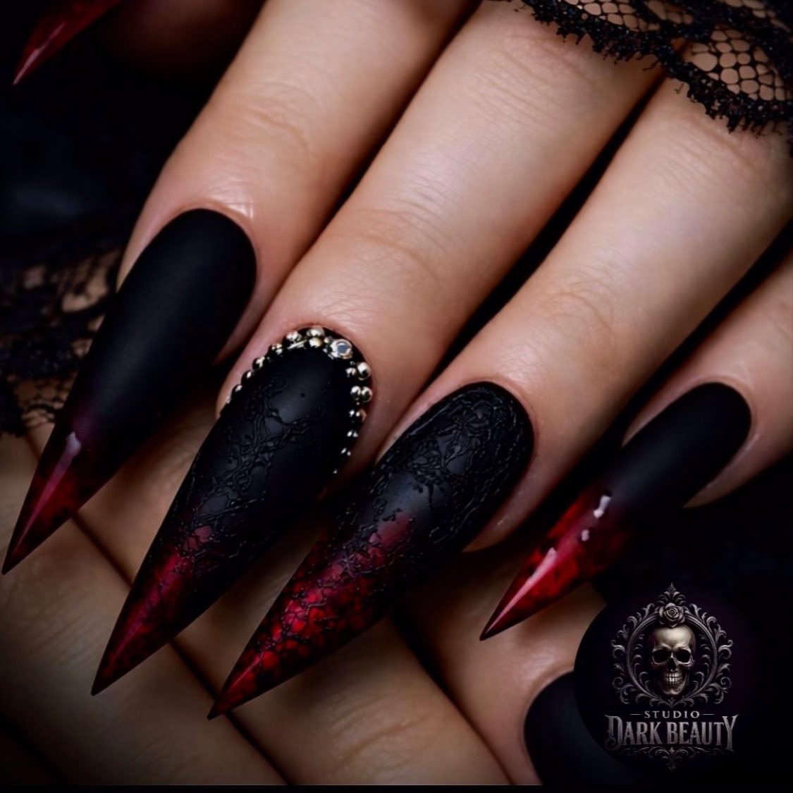 Long black stiletto nails are accented with deep red textured or glitter-like sections for a dark contrast.