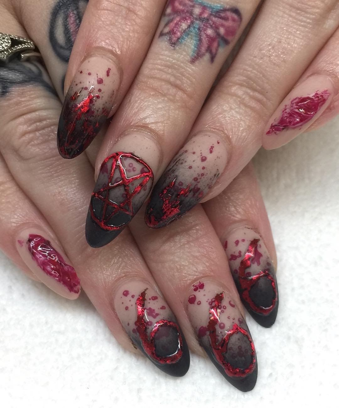 Sheer nude pointed nails feature black-and-red Halloween-style linework and decorative motifs.