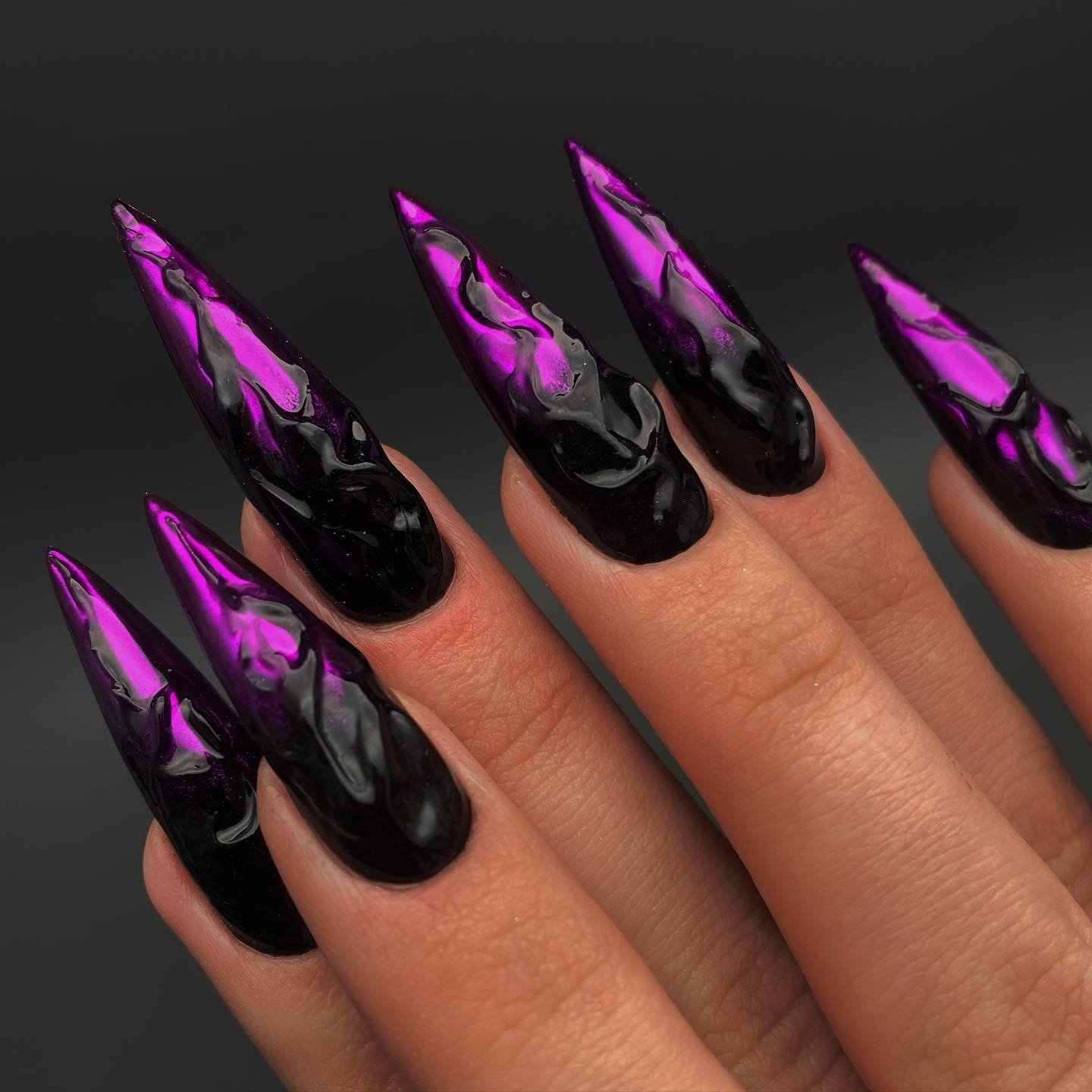 Long black stiletto nails are contrasted by vivid pink-purple flame-like shapes along the tips.