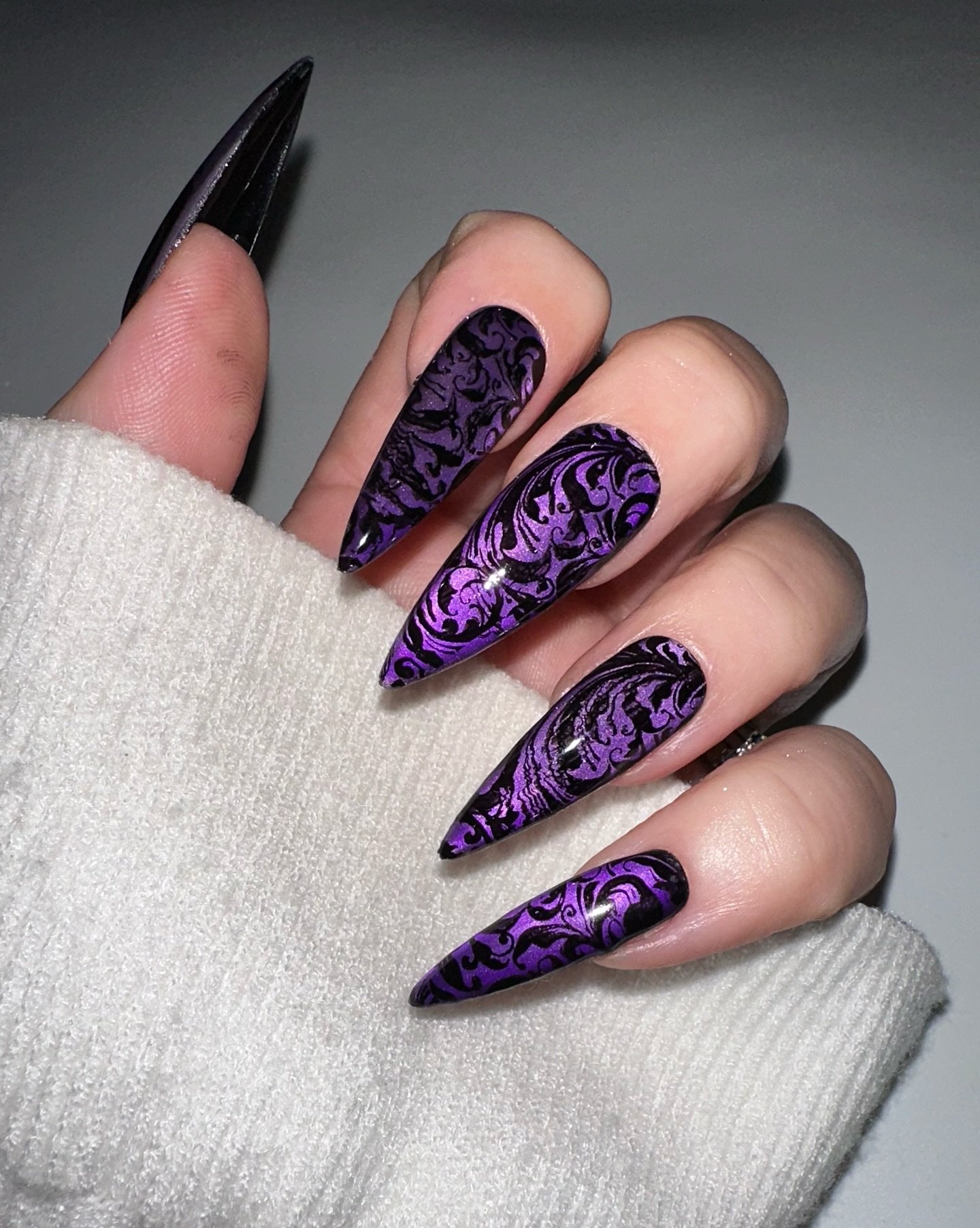 Pointed nails pair a black base with vivid purple textured patterns and intricate dark linework.