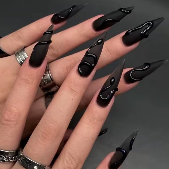 Long black stiletto nails feature sculpted-looking black raised designs that create a dramatic dimensional finish.
