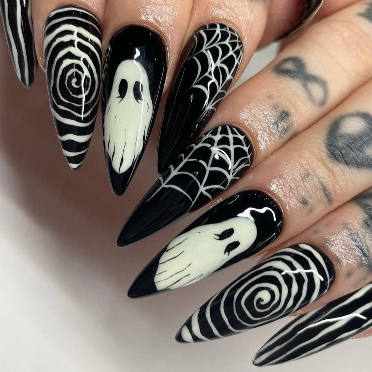 Pointed black-and-white nails combine ghost faces, spiderwebs, and hypnotic circular patterns.