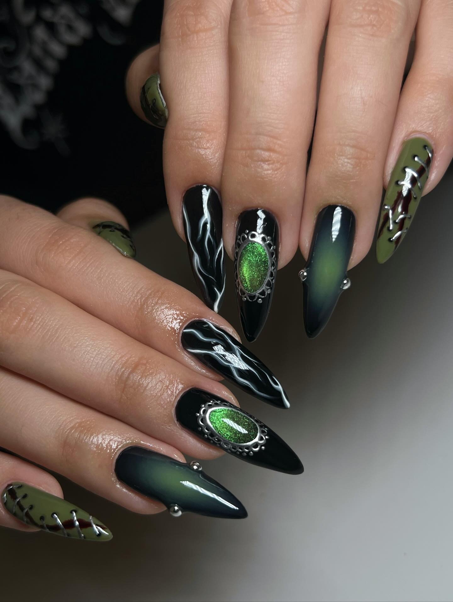 Long pointed nails blend black with deep green accents and metallic-looking green decorative details.