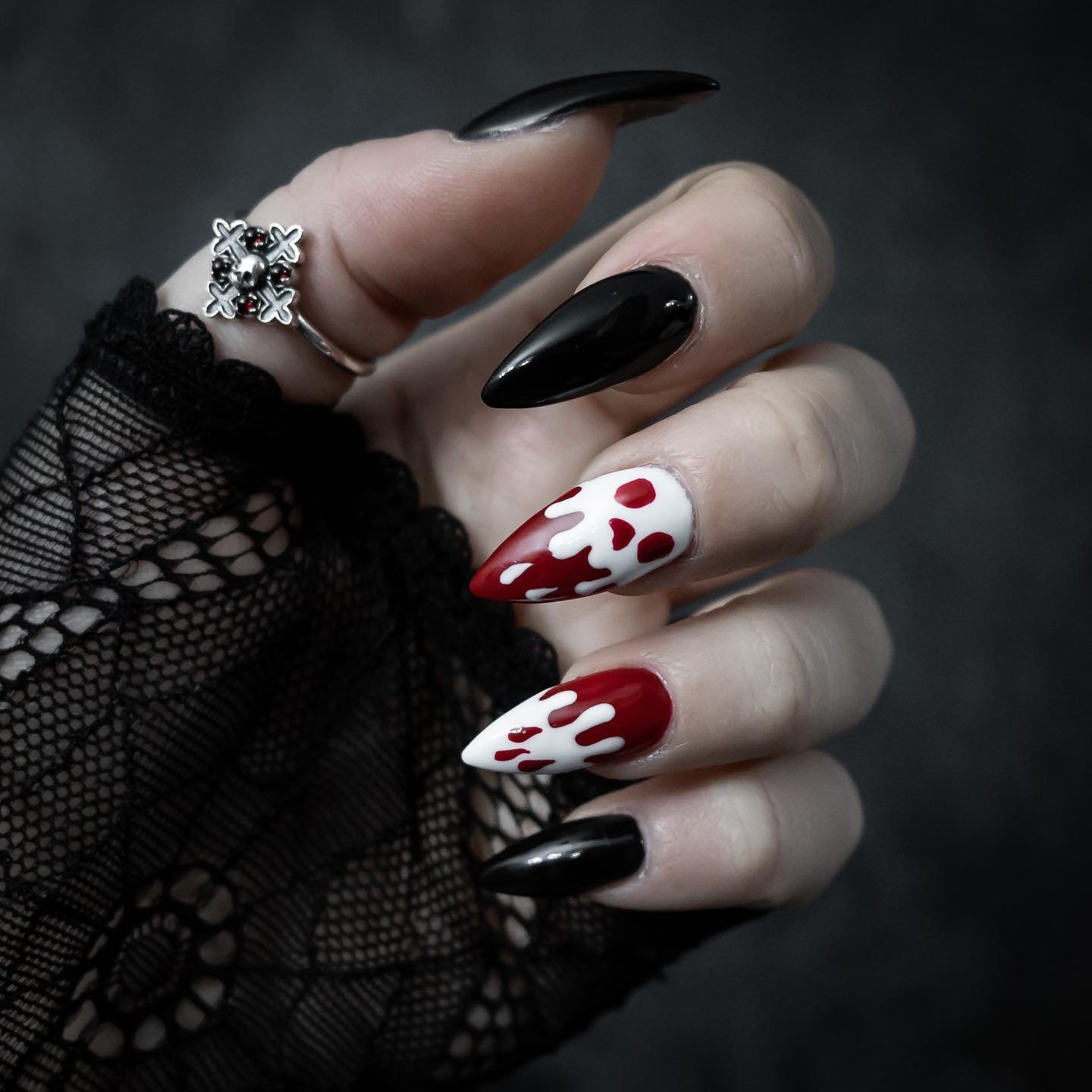 Black pointed nails are paired with white sections and vivid red drip-like details for a Halloween manicure.