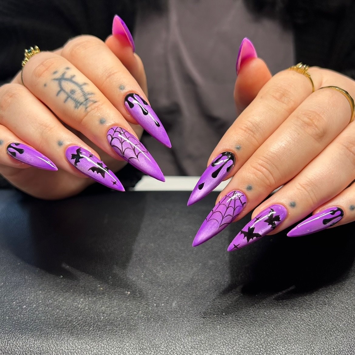 Long vivid purple stiletto nails feature black graphic linework and small decorative accents.