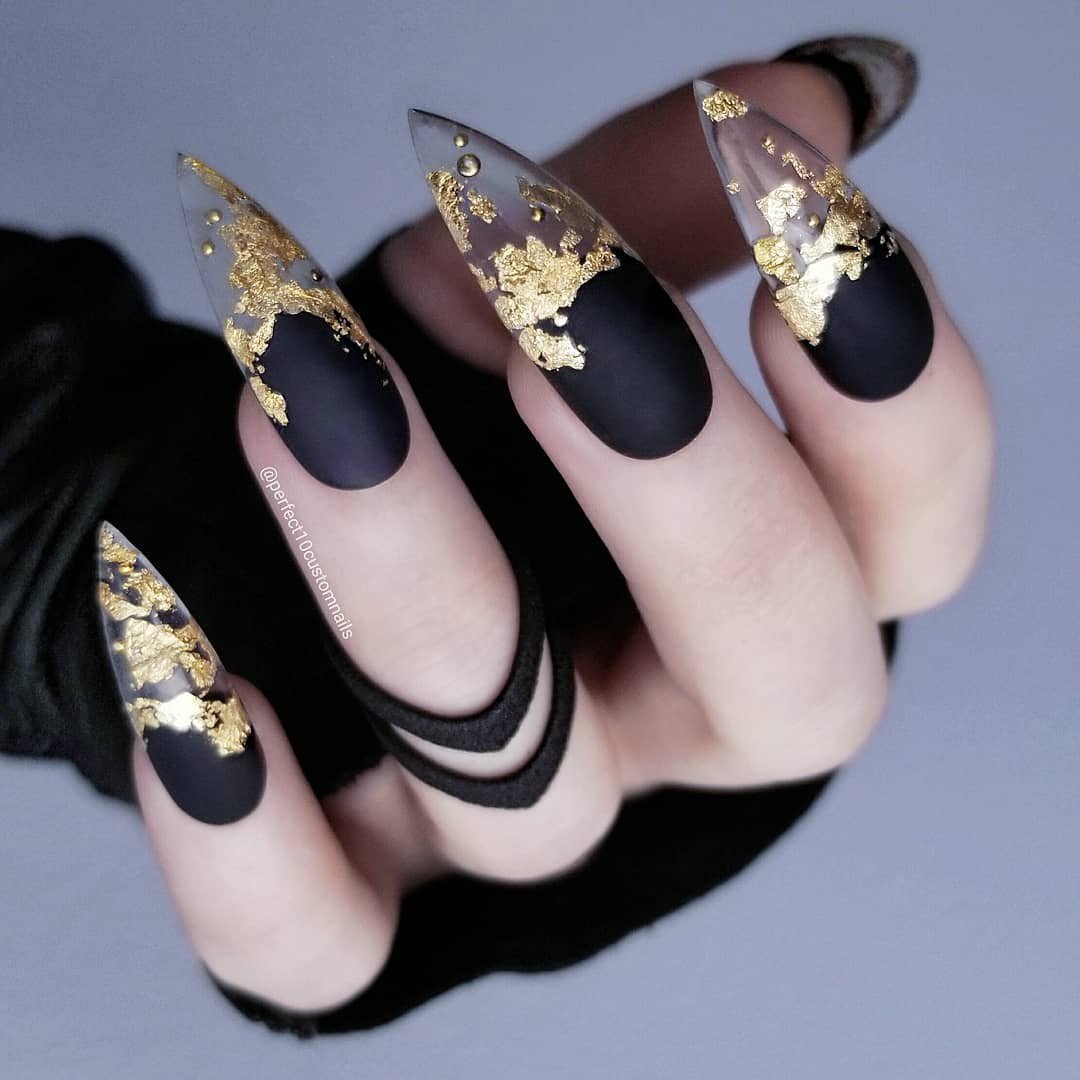 Matte black nails use pale negative space with sweeping black French tips and irregular gold foil accents.